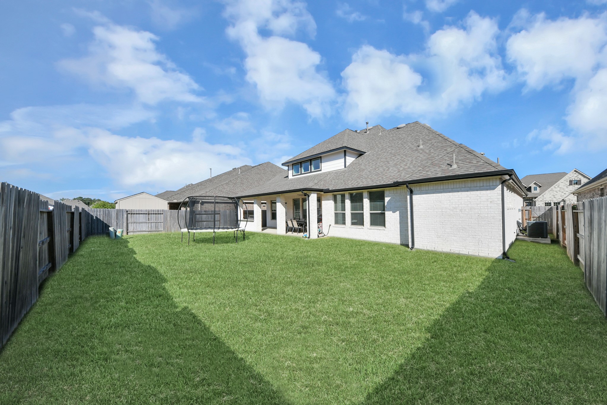 Spacious fenced backyard with lush green grass and a covered patio, perfect for outdoor activities and relaxation.