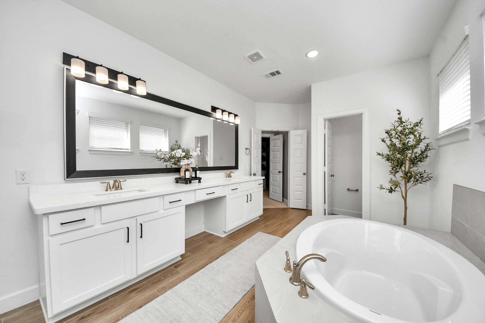 Spacious and elegant primary bathroom featuring a double vanity with sleek fixtures, a large mirror, and a luxurious soaking tub set against a backdrop of neutral tones and natural light.