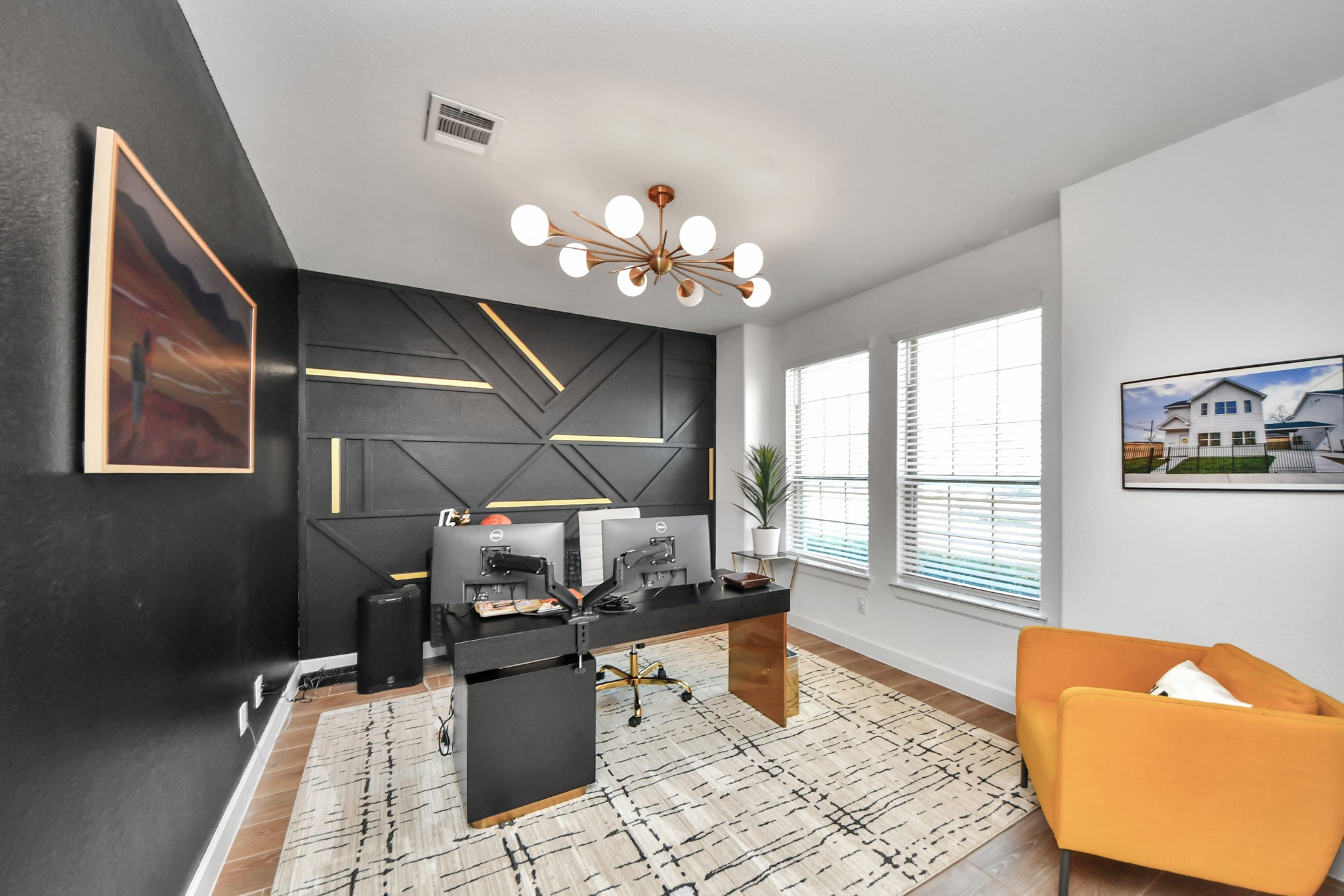 Chic home office with modern geometric accent wall, stylish lighting, and ample natural light from large windows.