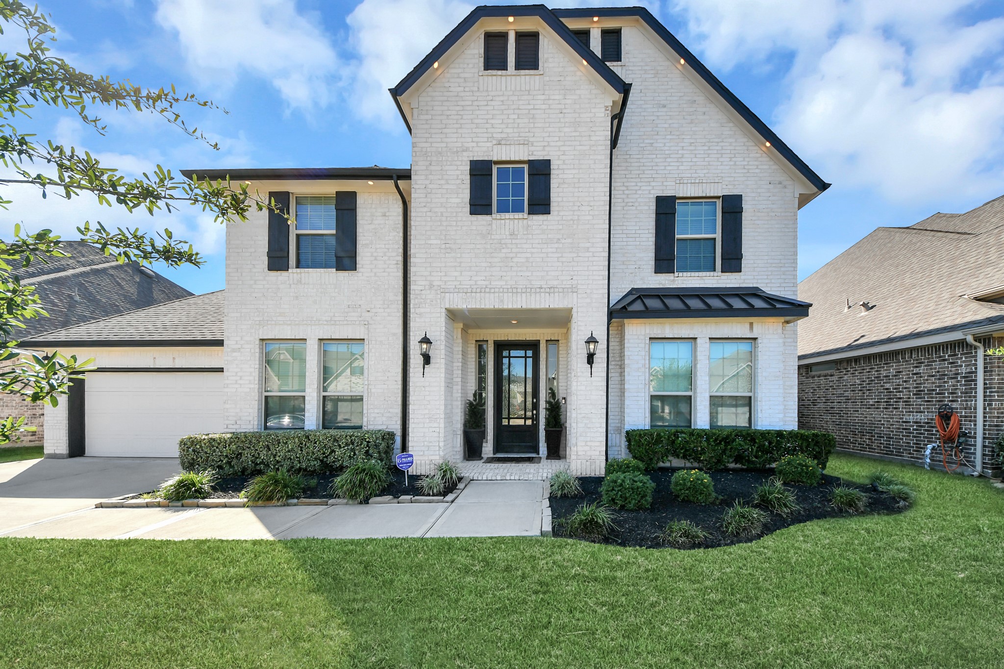 Stunning two-story home with elegant white brick faade, charming black shutters, and a beautifully landscaped front yard.