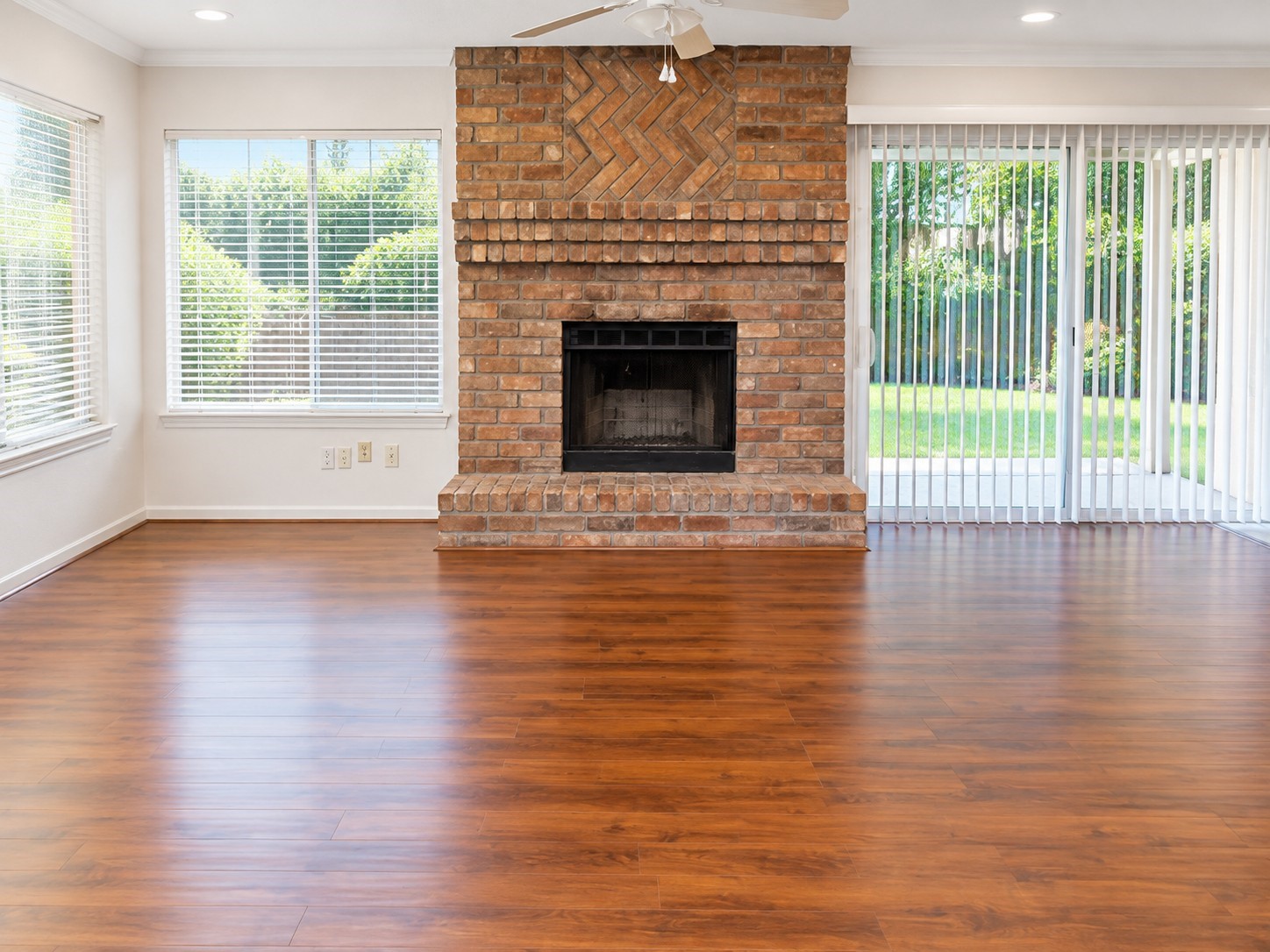 Spacious living area with wood flooring, brick fireplace, and natural light.