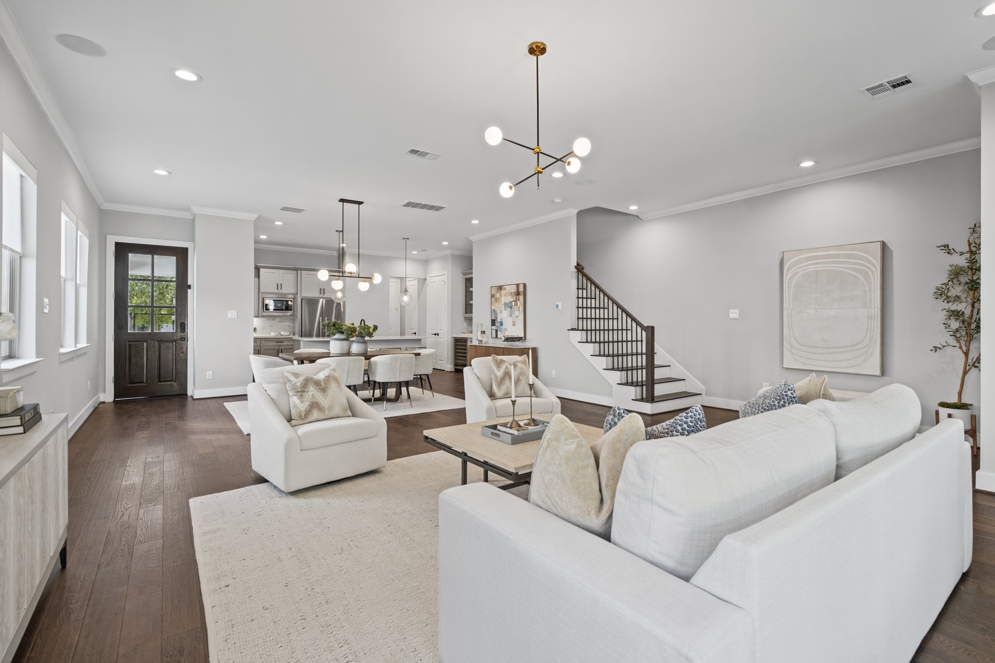 Generously scaled and beautifully light-filled, the living room features warm wood floors, neutral furnishings, and a striking staircase that adds architectural interest.