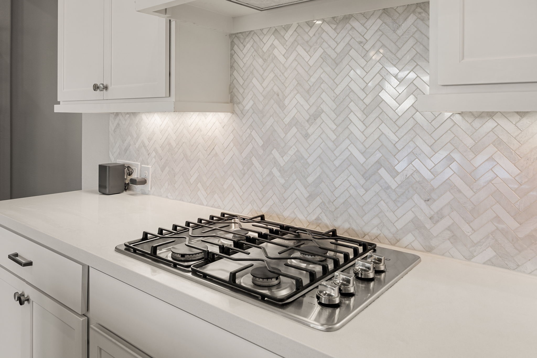 Attention to detail shines in this culinary corner, featuring a premium five-burner gas cooktop integrated seamlessly into the quartz countertops. A striking marble herringbone backsplash serves as a gorgeous focal point, beautifully highlighted by custom under-cabinet task lighting.