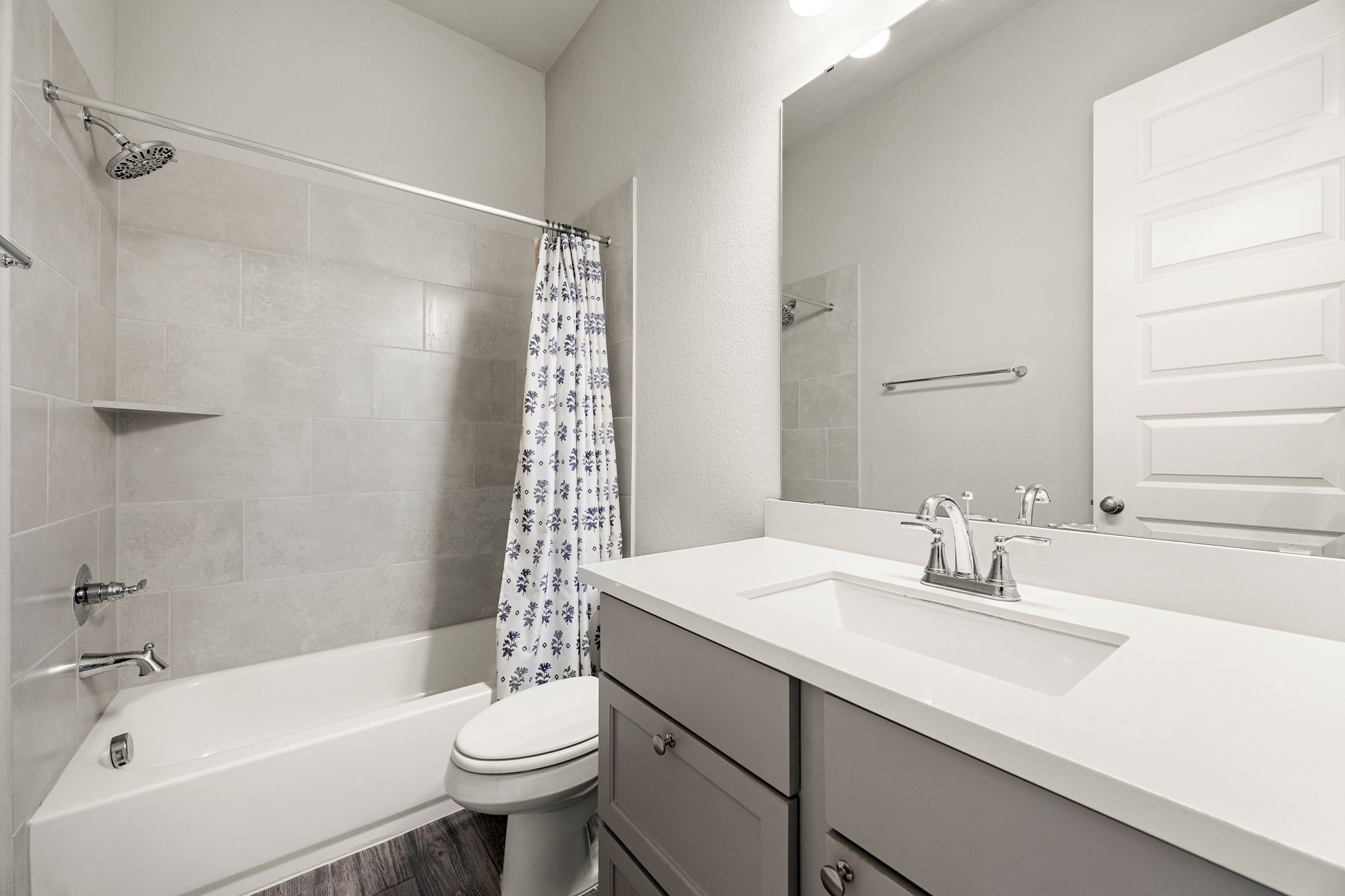 The pristine secondary bathroom features a stylish gray vanity with a crisp white undermount sink and a smooth engineered countertop. Perfect for family or guests, the space includes a full tub/shower combination beautifully finished with large-format tile surround that stretches to the ceiling, all tied together by durable wood-look flooring.