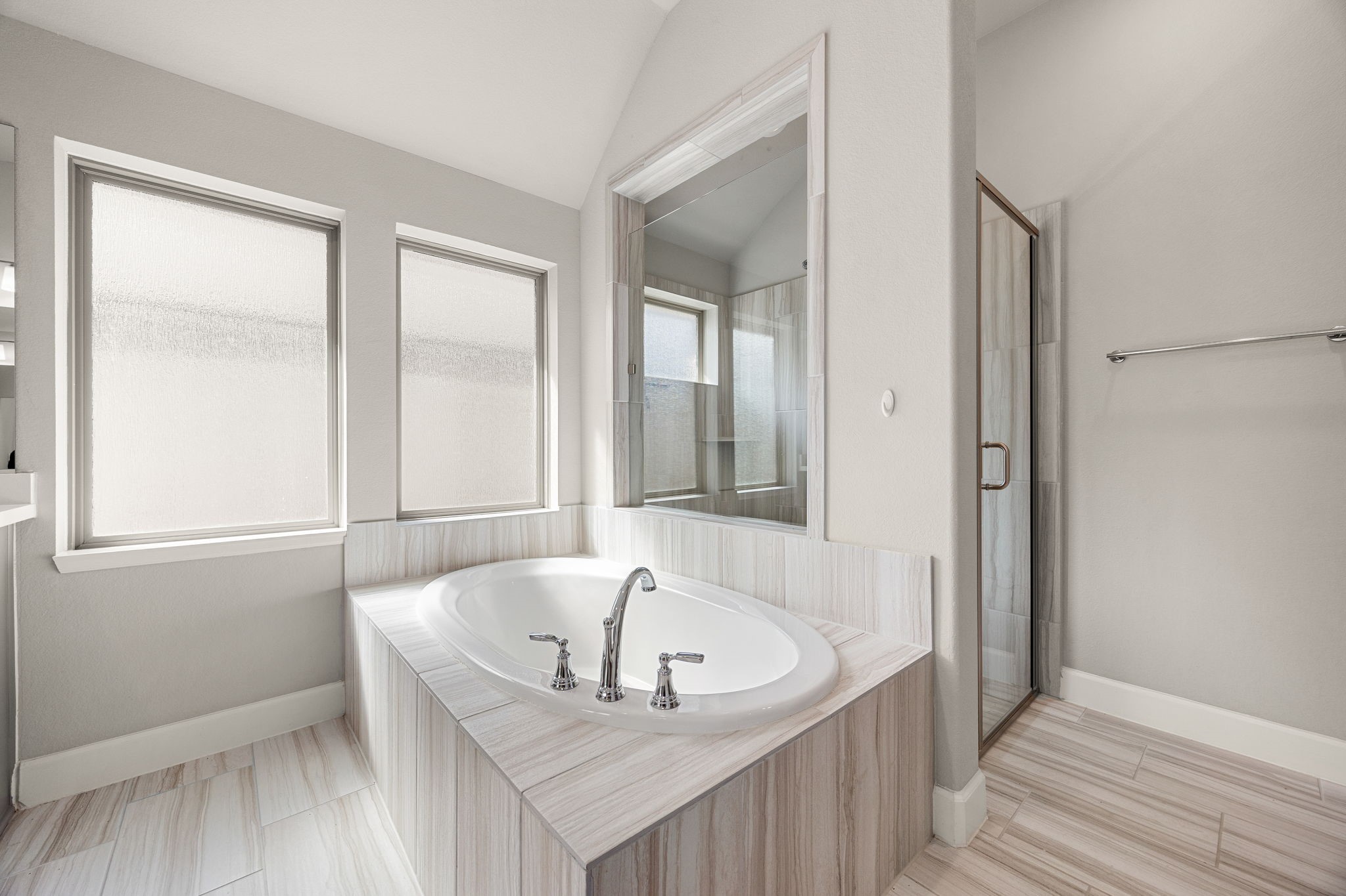 This peaceful sanctuary is designed for pure relaxation. The beautiful tile flooring flows seamlessly up the base of the luxurious garden tub, while a unique glass partition looks directly into the standalone shower, enhancing the bright, open, and architectural feel of the entire suite.