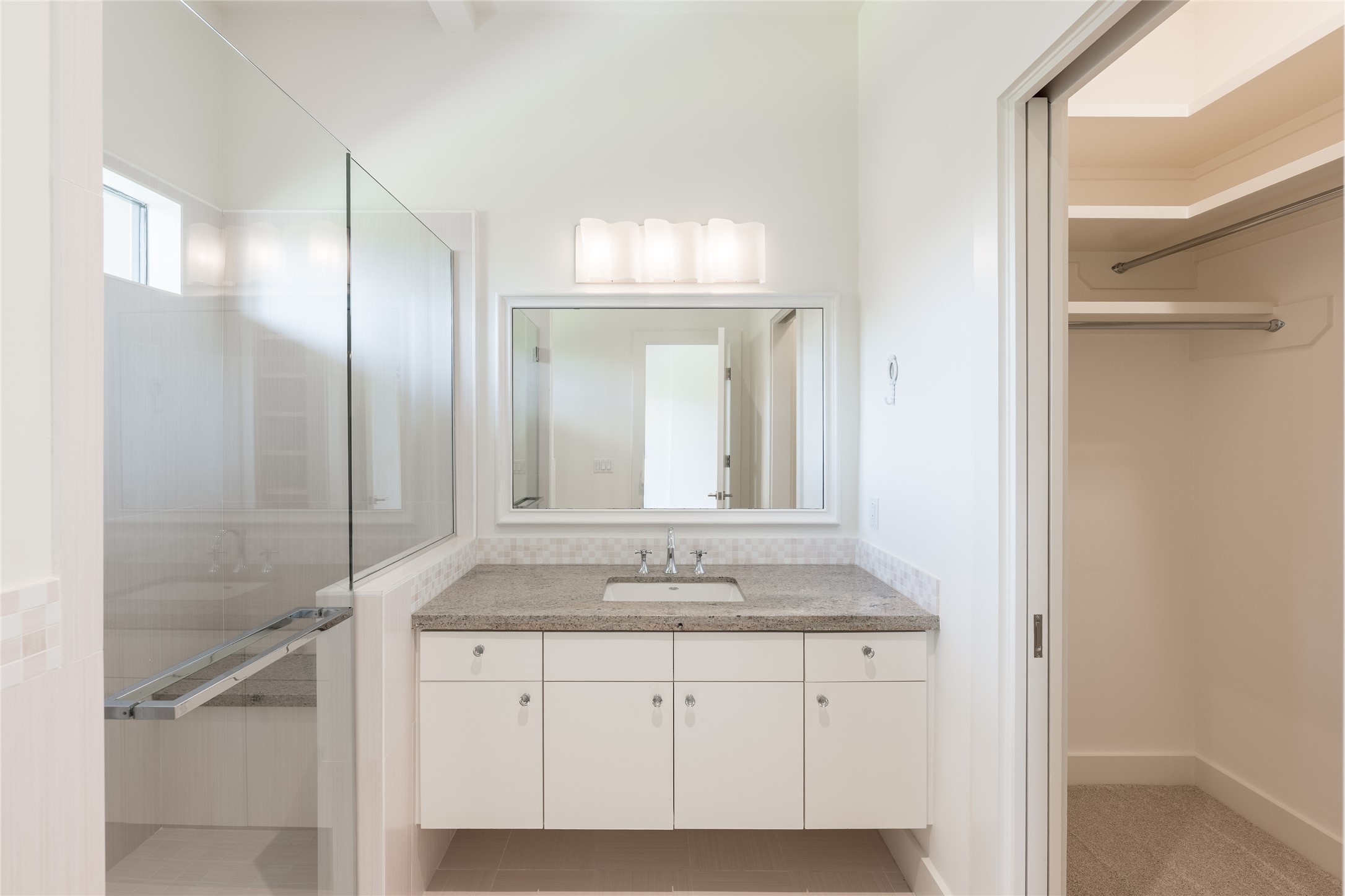 The secondary bedroom is complete with its own private ensuite bath, featuring a floating vanity, full-width mirror, glass-enclosed walk-in shower and dedicated closet space.