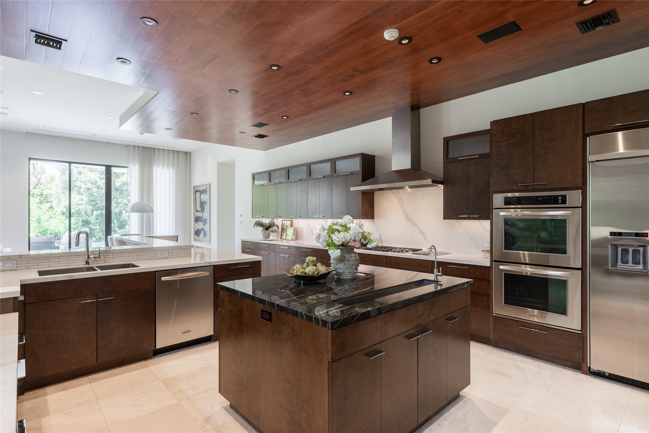 At the center of the kitchen, a dedicated prep island incorporates a linear sink and contrasting dark countertop, creating a striking counterpoint to the lighter porcelain surfaces surrounding it.