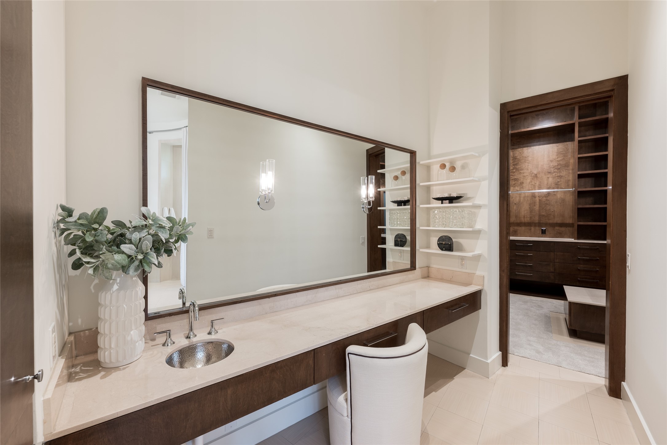 A dedicated vanity within the primary ensuite provides its own defined space, featuring custom floating cabinetry, an expansive mirror and sconces. The generous counter surface and floating shelves keep the area both functional and refined.