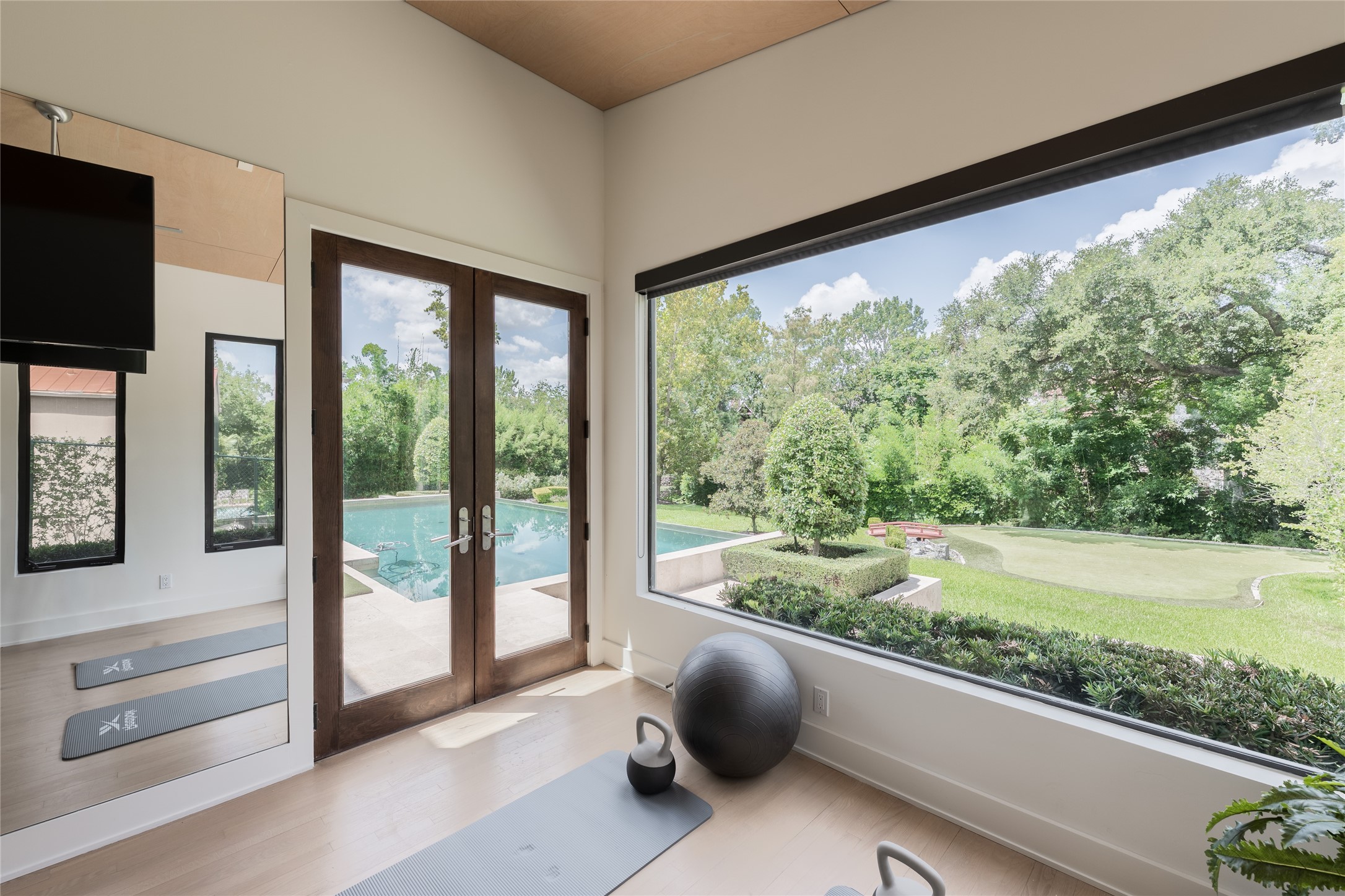 A second perspective of the wellness studio highlights its connection to the grounds, with oversized windows capturing views of the pool, putting green and mature landscaping. Glass doors provide direct outdoor access, extending the space naturally into the backyard.