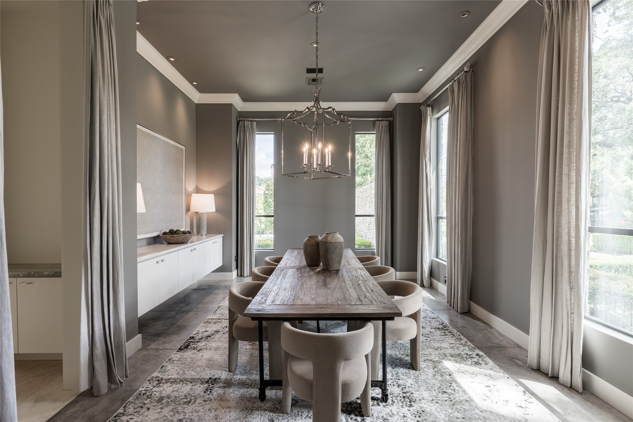 The formal dining room unfolds across from the study, framed by floor-to-ceiling windows dressed in custom curtains that soften the natural light. A sculptural chandelier anchors the elongated space, creating an elegant setting for intimate dinners or larger gatherings.
