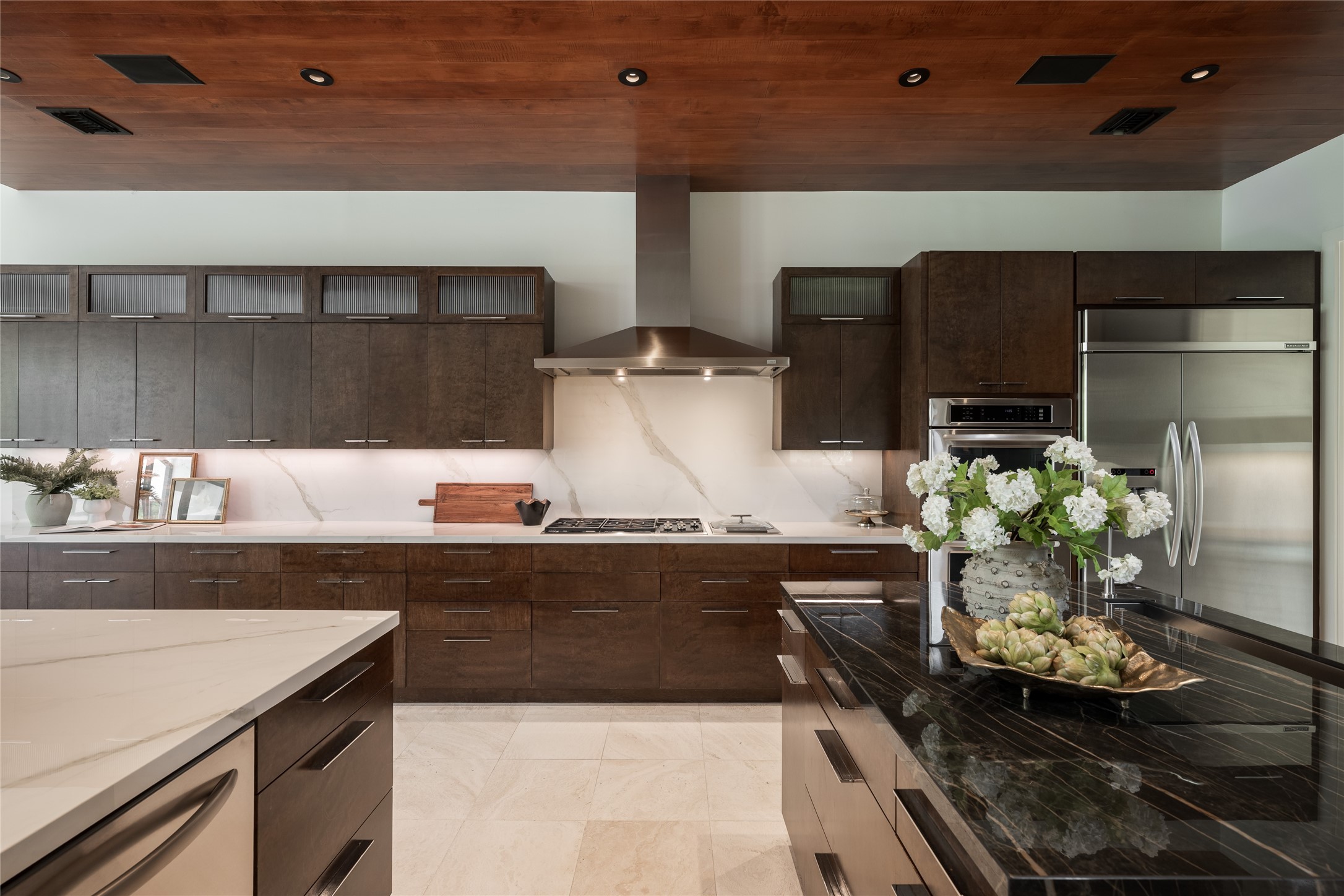 The kitchen pairs craftsmanship with integrated technology, featuring custom LED lighting and built-in surround sound speakers throughout the kitchen. A Wolf range and double ovens, Sub-Zero refrigerator and porcelain backsplash complement the custom cabinetry.