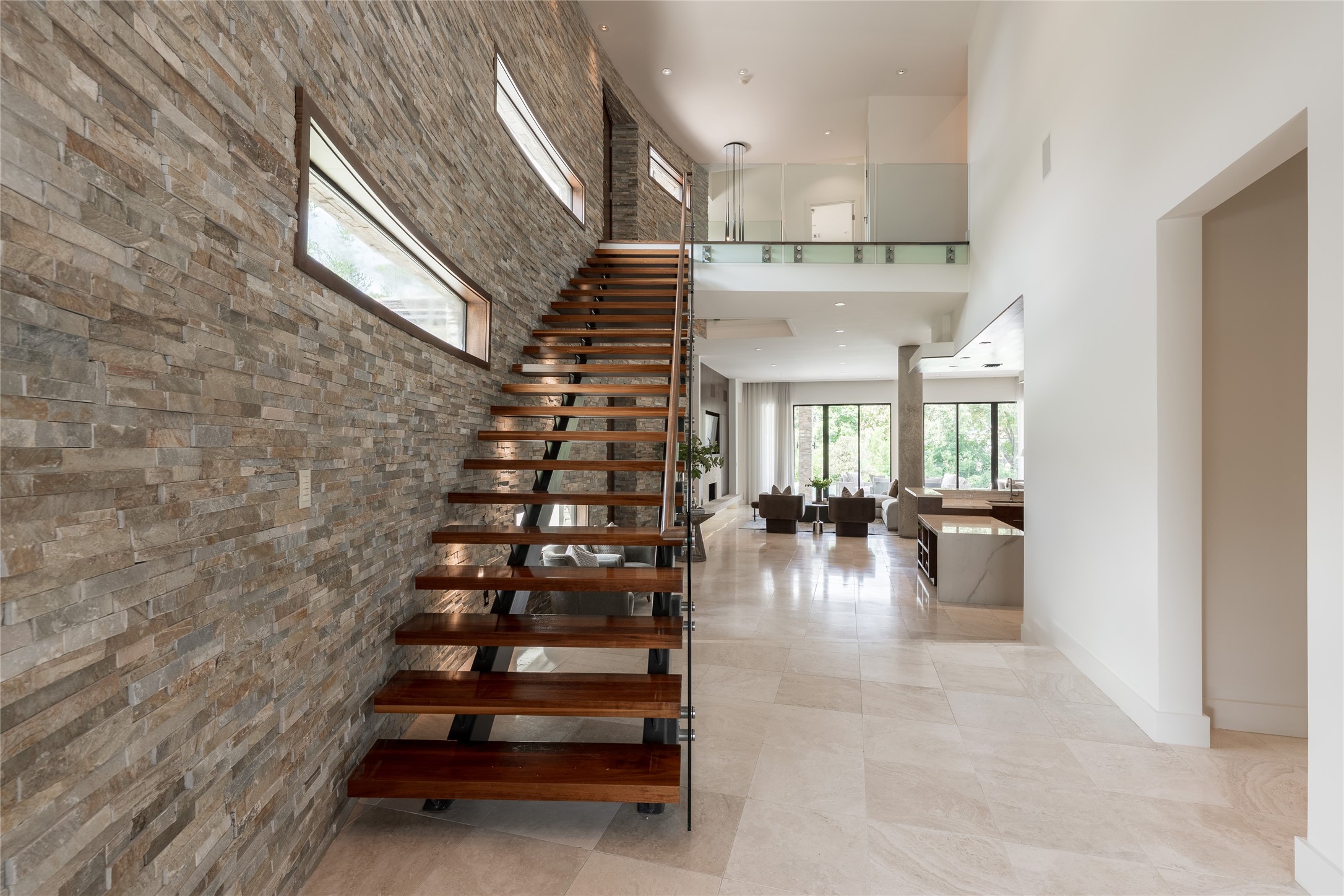 The homes signature curved stacked-stone wall continues along the staircase, creating a strong architectural feature between levels. Floating walnut stair treads extend from the stone with an open-riser design, pairing two of the homes defining natural materials in one sculptural element.