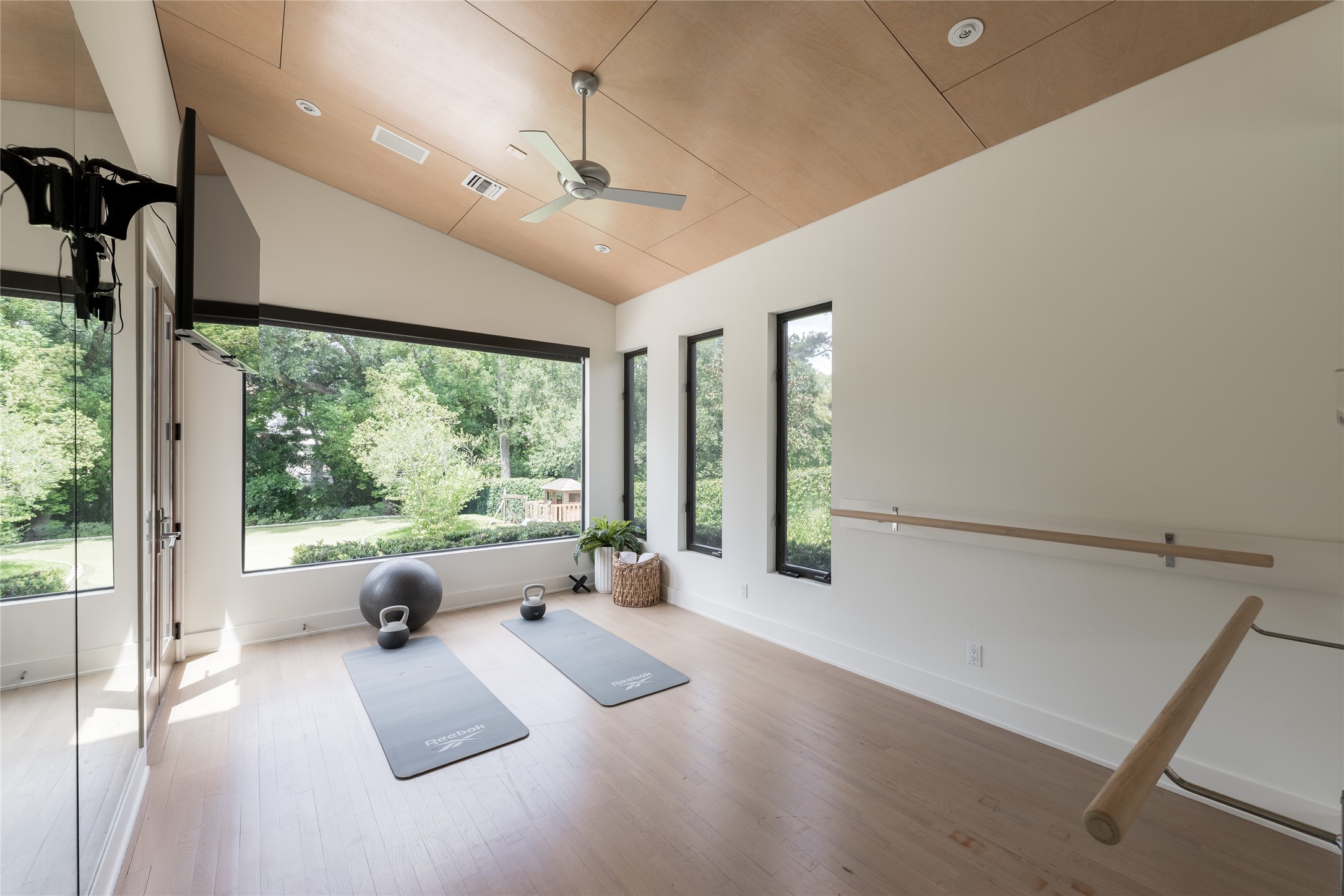 A dedicated wellness studio offers space for yoga, stretching or private training, complete with a built-in ballet barre and mirrored wall. Oversized windows frame views of the backyard and putting green, while the wood-paneled ceiling adds warmth to the light-filled space.