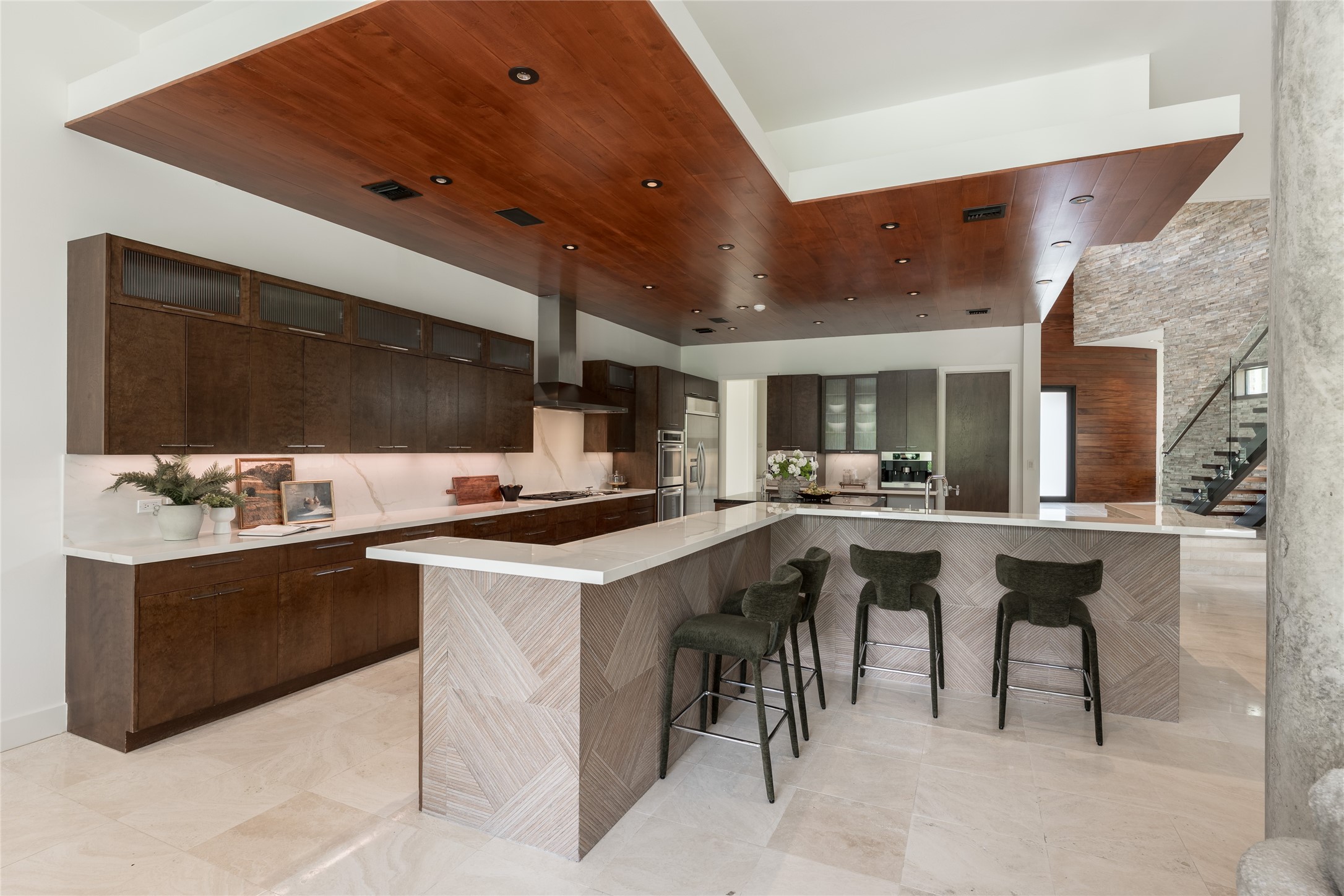 The expansive tabletop island is finished with a distinctive patterned tile, adding another layer of custom design to the kitchen. Cabinet upper display cabinetry frames an impressive stretch of back counterspace, while this angle begins to reveal the suite of high end appliances integrated throughout the kitchen.