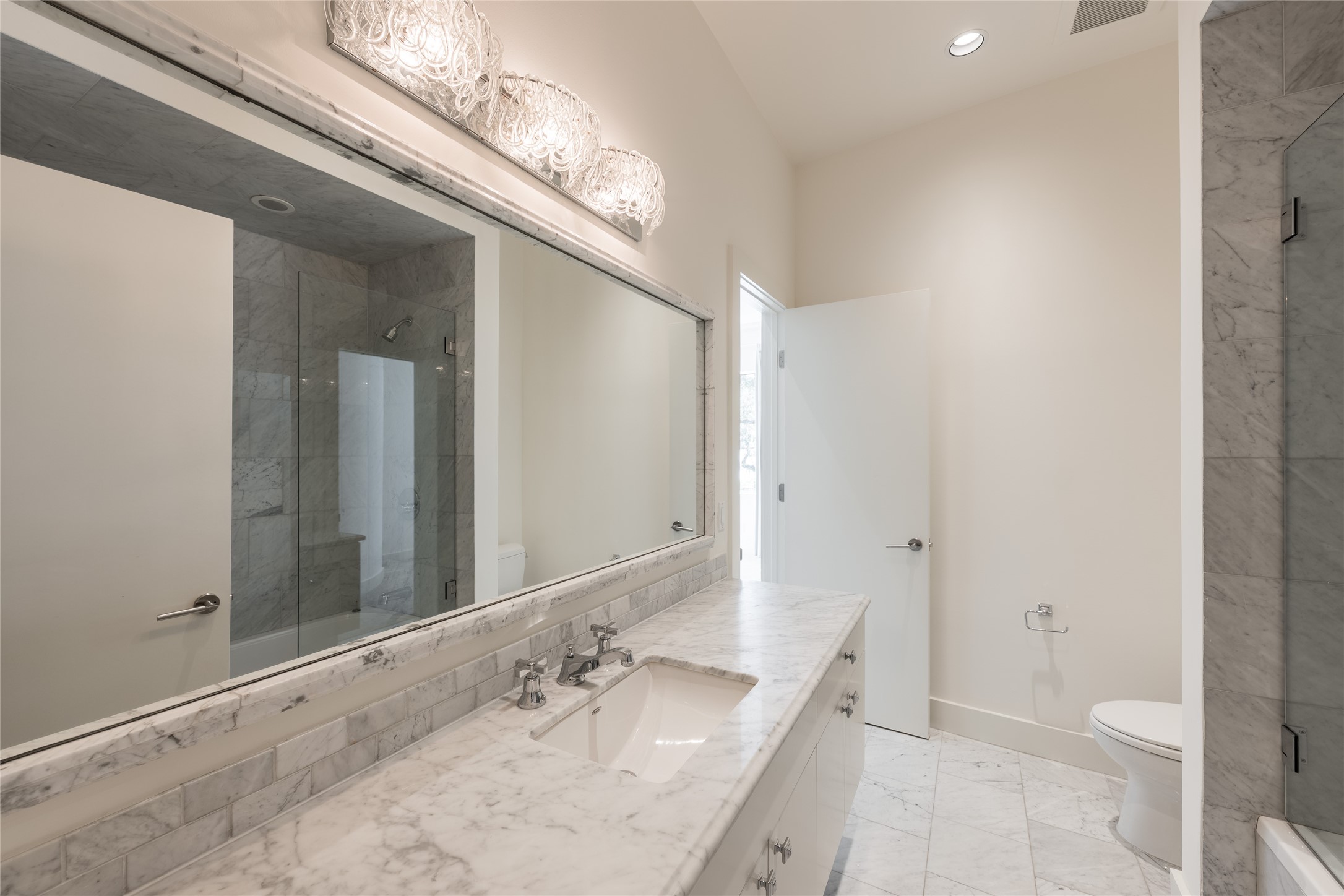 full ensuite bath, featuring an expansive vanity with generous counterspace, a full-width mirror and a glass-enclosed walk-in shower/tub.