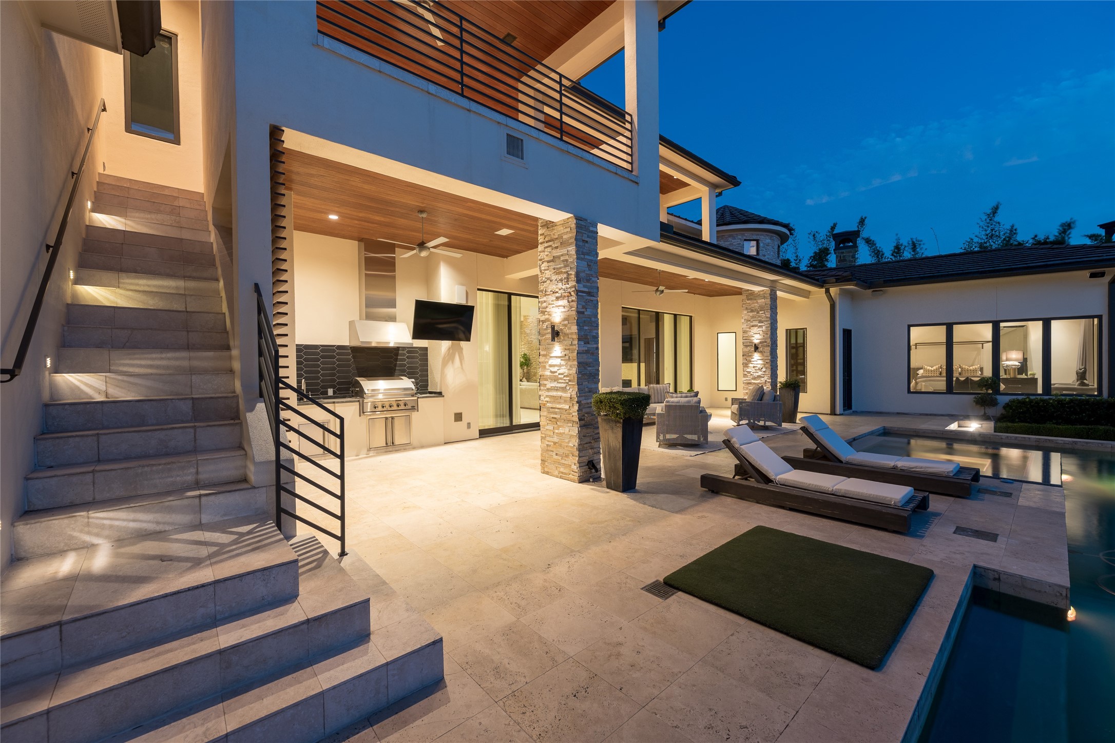 At dusk, the second covered outdoor living area reveals another layer of the homes entertaining space, with direct access from the main residence and pool. An exterior staircase provides a separate connection to the second floor, while integrated lighting allows the outdoor areas to transition seamlessly into the evening.