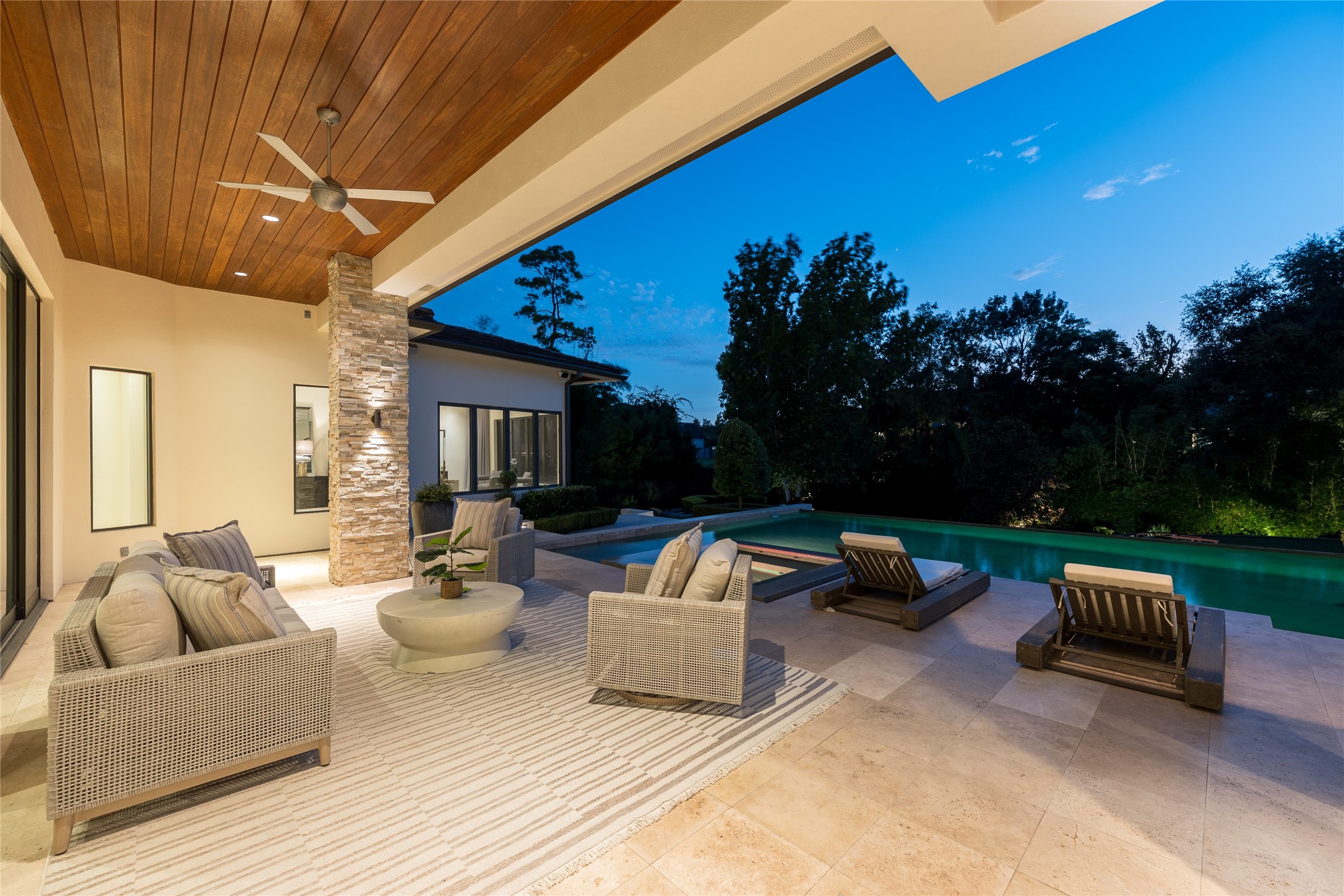 The first-floor covered outdoor living area creates a separate lounge setting beside the heated saltwater pool, finished with a mahogany tongue-and-groove ceiling and travertine flooring. Integrated pool lighting extends the setting into the evening, while the covered space provides a direct extension of the homes indoor living areas.