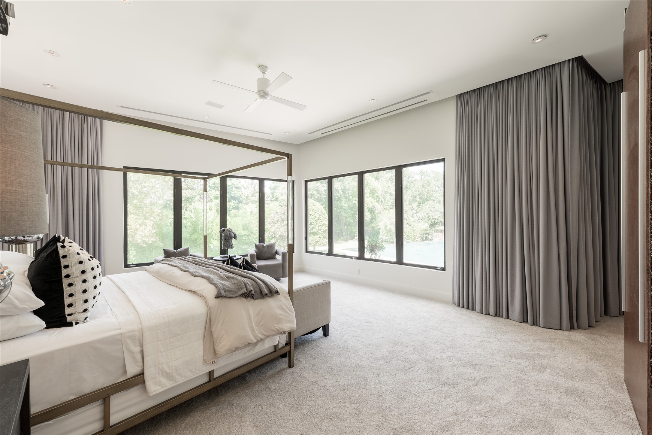The first-floor primary suite is positioned to capture views across the landscaped backyard and pool, with corner windows bringing the grounds into view from multiple angles. A concealed motorized projector screen and integrated surround sound transform the space for entertainment while remaining discreet when not in use