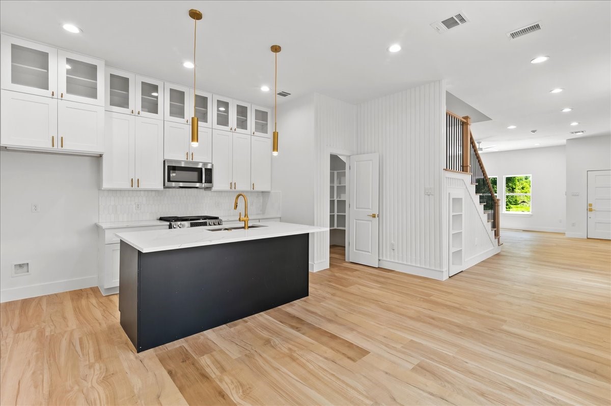 Unit A - Designer kitchen featuring double-stacked white cabinetry, a striking black accent island, elegant gold fixtures, and stainless steel appliances, blending modern sophistication with everyday functionality. Accent Wall design may vary. Pictures are from a previous build.