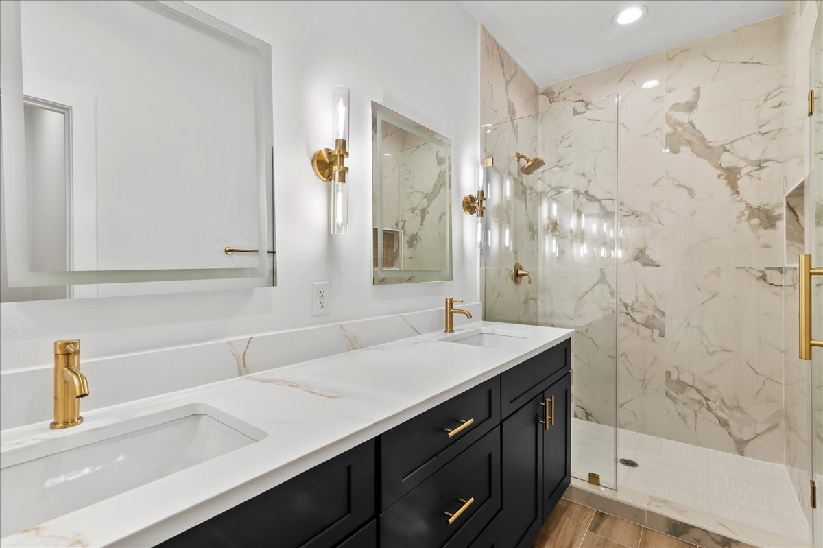 Unit A - Luxurious primary suite bathroom featuring a spacious walk-in shower with elegant gold fixtures, dual vanities, and LED mirrors, creating a sophisticated spa-like retreat.