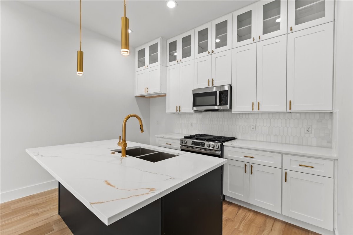 Unit A - Enjoy a sleek, modern kitchen featuring a flat-top stove, stainless steel appliances, elegant gold fixtures, and designer finishes throughout.