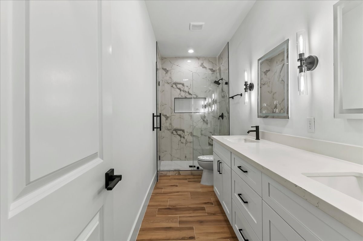 Unit B - Stylish primary bath is equipped with dual vanities, LED mirrors, and walk-in shower with ceramic tile surround.