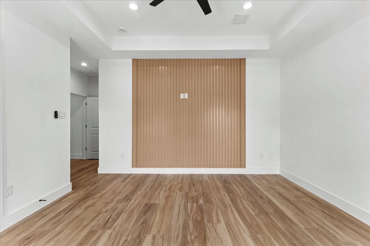 Unit B - Spacious primary suite featuring a beautiful neutral-toned accent wall that perfectly complements the wood-look flooring, elegant coffered ceiling, and a remote-controlled ceiling fan. Accent Wall design may vary. Pictures are from a previous build.