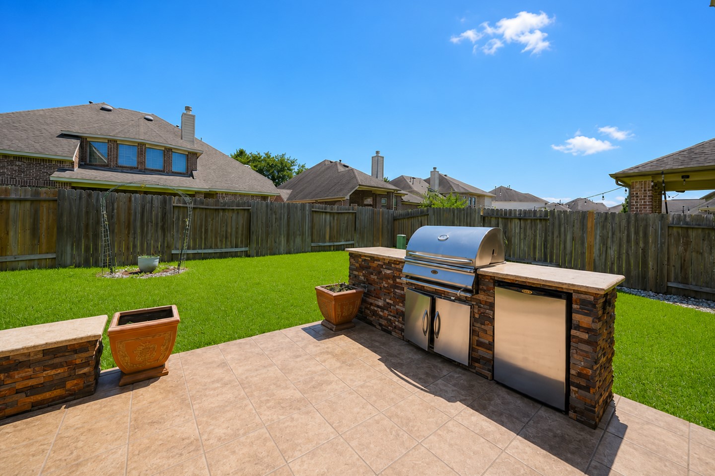 Spacious backyard with a tiled patio featuring an outdoor grill and mini-fridge, perfect for entertaining. Well-maintained lawn and privacy fence enhance the outdoor living space.