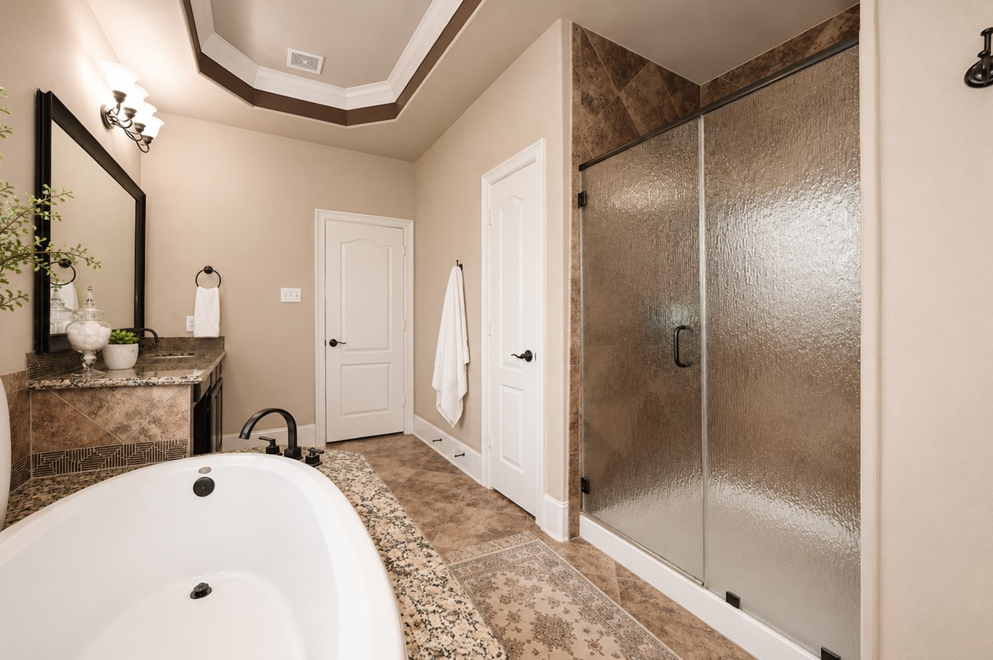 This elegant bathroom features a spacious layout with a luxurious soaking tub, a large glass-enclosed shower, and a dual-sink vanity with granite countertops. The neutral color scheme and detailed tile work add a touch of sophistication.
