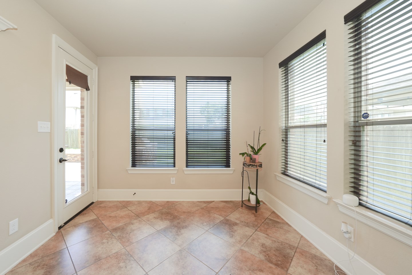 Bright space that extends from the kitchen with large windows featuring blinds, tiled floor, and a door leading outside. Perfect for plants or a cozy reading nook.