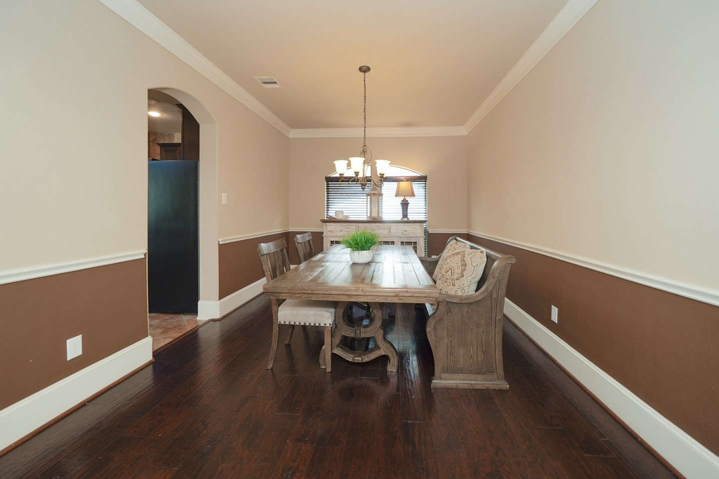 This dining room features elegant wood flooring, and warm two-tone walls with wainscoting. A chandelier adds a touch of sophistication, and an arched entry leads to the adjacent Kitchen entrance.