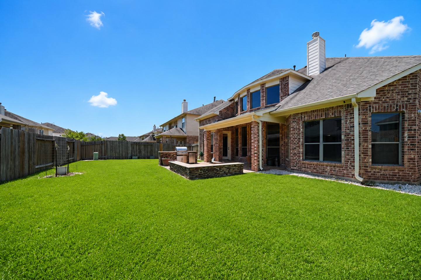 This photo shows the backyard of a brick house with a well-maintained lawn, a spacious patio area, and a wooden fence for privacy, perfect for outdoor activities and entertaining.