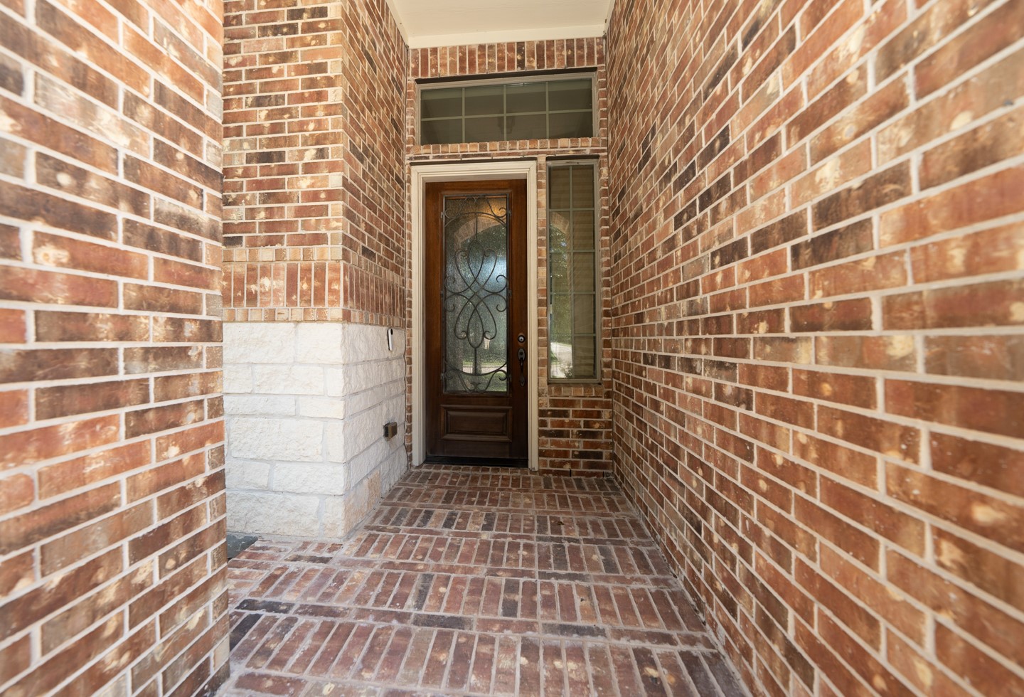 This photo showcases a welcoming entryway with a decorative wooden front door featuring glass panels. The surrounding walls and floor are made of red brick, offering a warm and classic look.