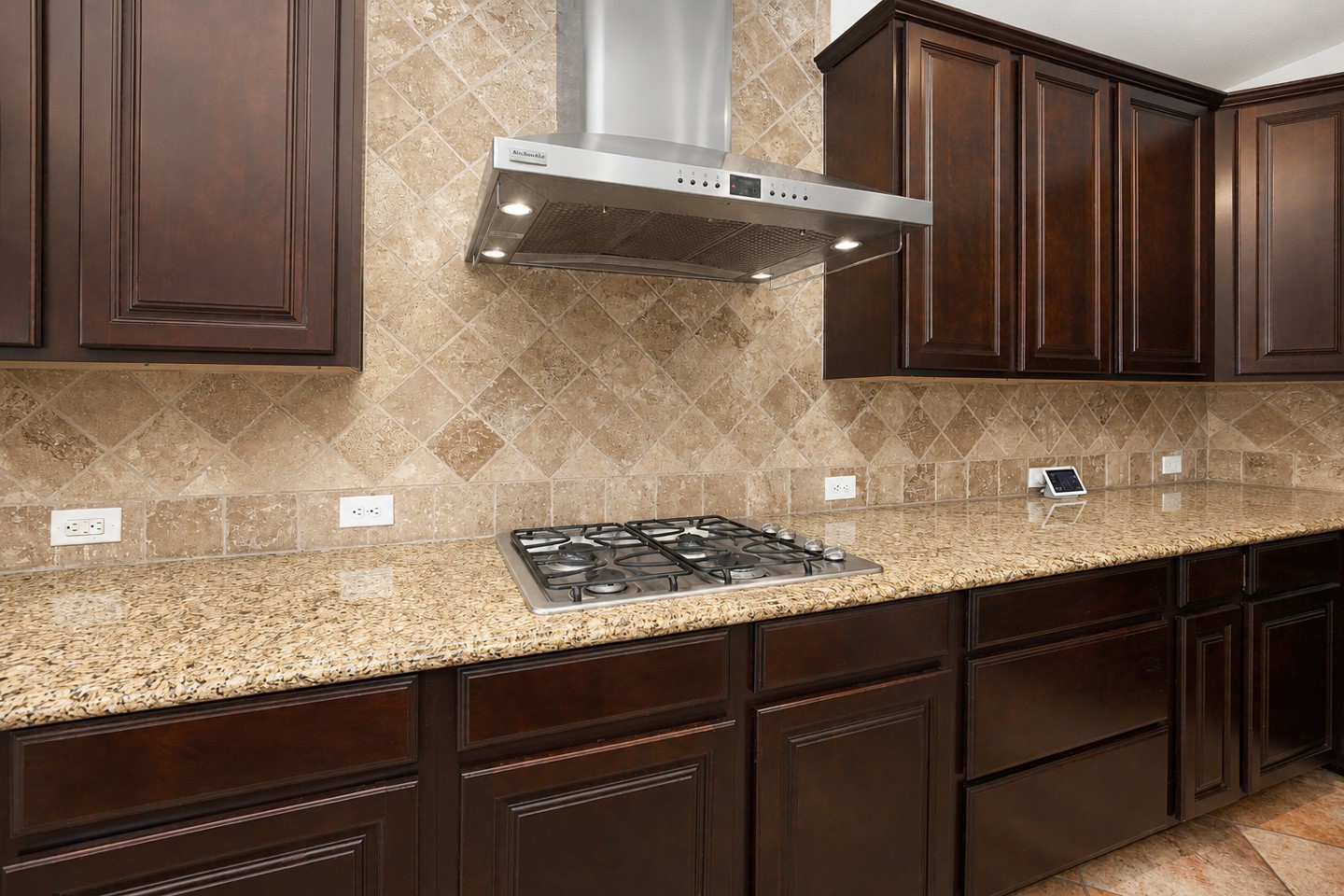 This kitchen features rich dark wood cabinets, a sleek stainless steel range hood, granite countertops, and a stylish tiled backsplash, offering a blend of elegance and functionality.