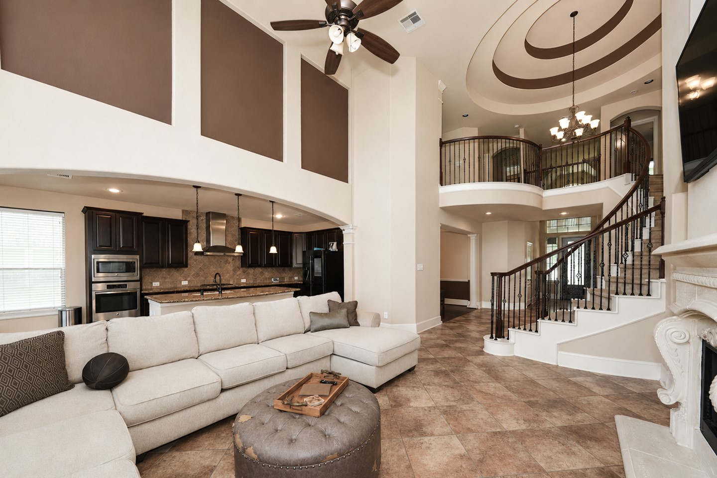 This spacious living area features a high ceiling with two toned color walls bringing life to this bright and open living. Great floorplan connecting to a modern kitchen with dark cabinetry, and a sweeping staircase with wrought iron railings. The room is adorned with tile flooring, creating a warm, inviting atmosphere.