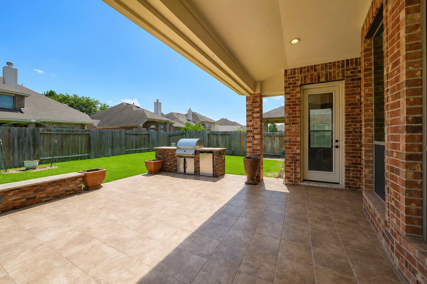This photo showcases a spacious covered patio with tile flooring, a built-in grill, and a view of a well-maintained fenced backyard. Perfect for outdoor entertaining and relaxation.