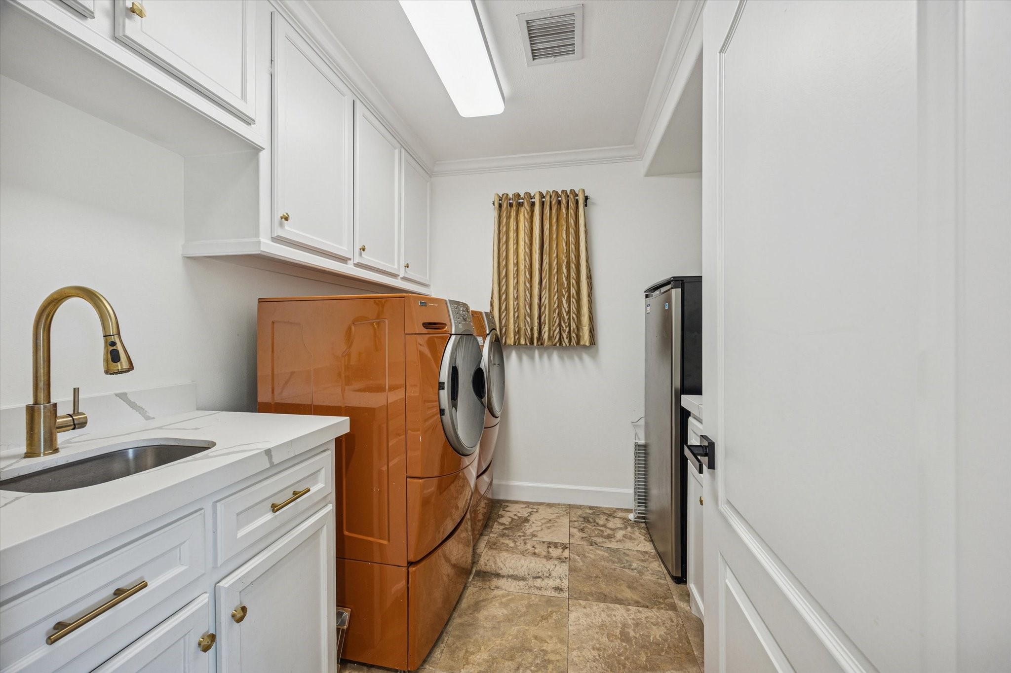 Spacious laundry room with ample cabinetry for storage, a sink with a modern faucet. There is room for another refrigerator or freezer in this space.