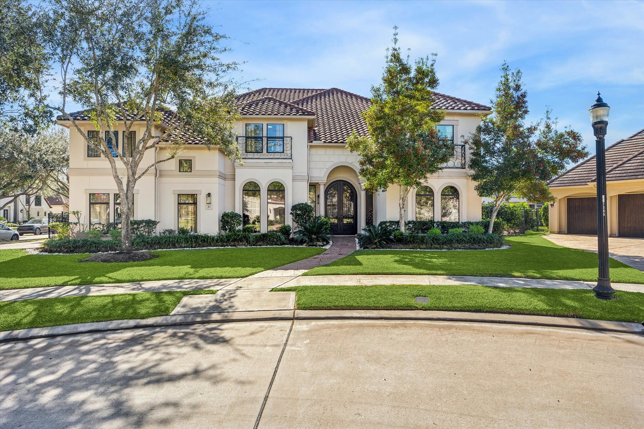 This stunning two-story home features a Mediterranean-inspired design with a tiled roof and arched windows. The manicured front lawn, framed by mature trees and lush landscaping, enhances its curb appeal. A spacious driveway leads to a three-car garage, offering ample parking and storage.