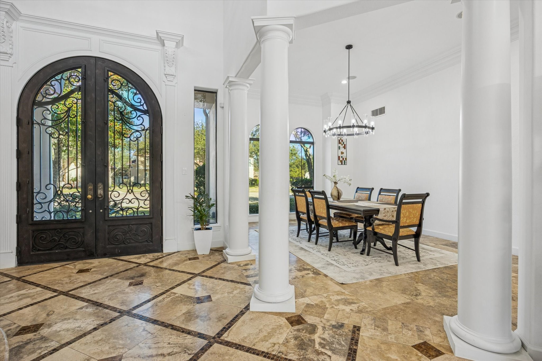 Elegant entryway with ornate double doors and a spacious dining area. Features high ceilings, decorative columns, and tile flooring, creating a luxurious and inviting atmosphere.