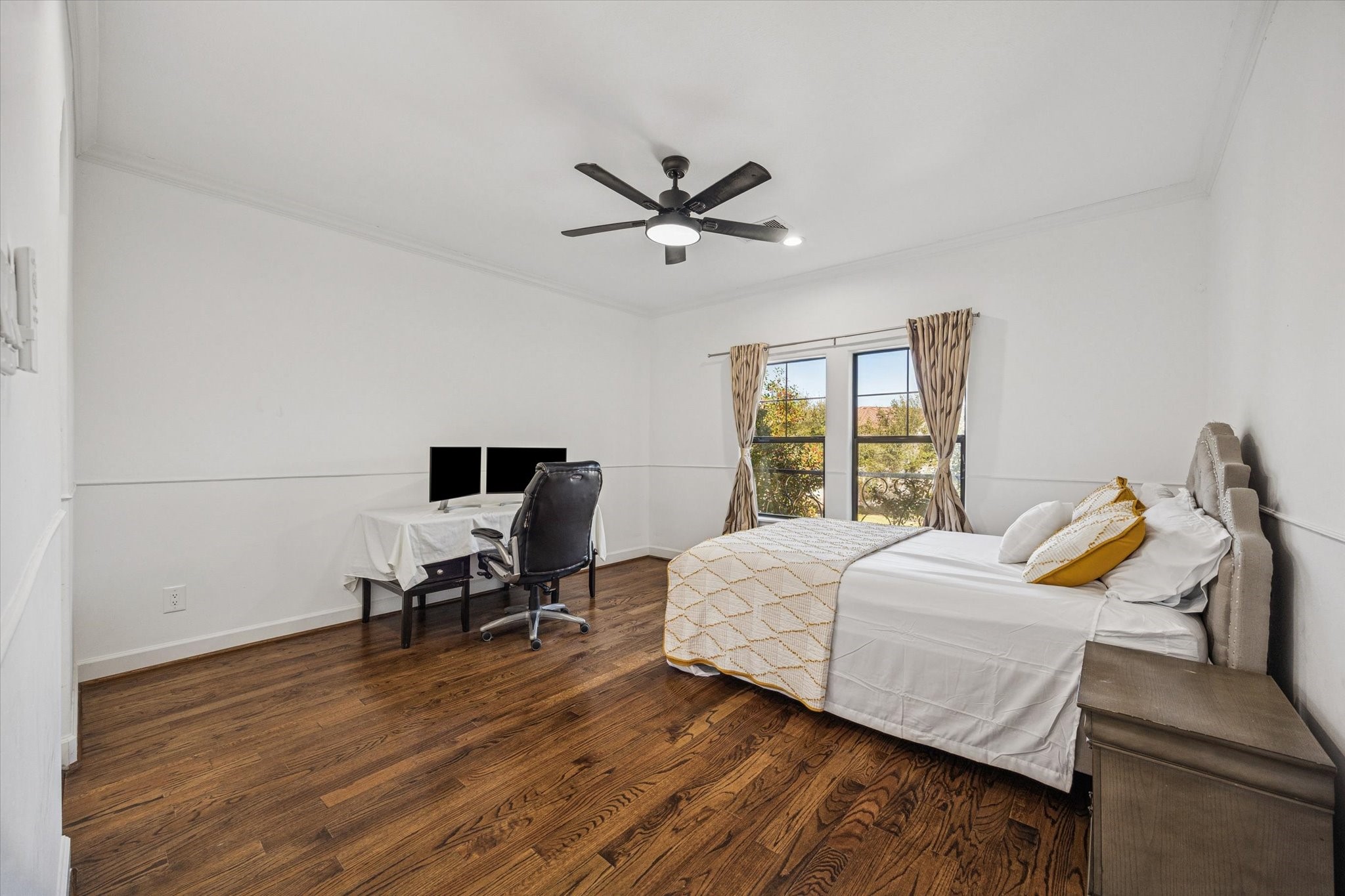 This spacious bedroom features hardwood floors, a large window with natural light, and a modern ceiling fan.