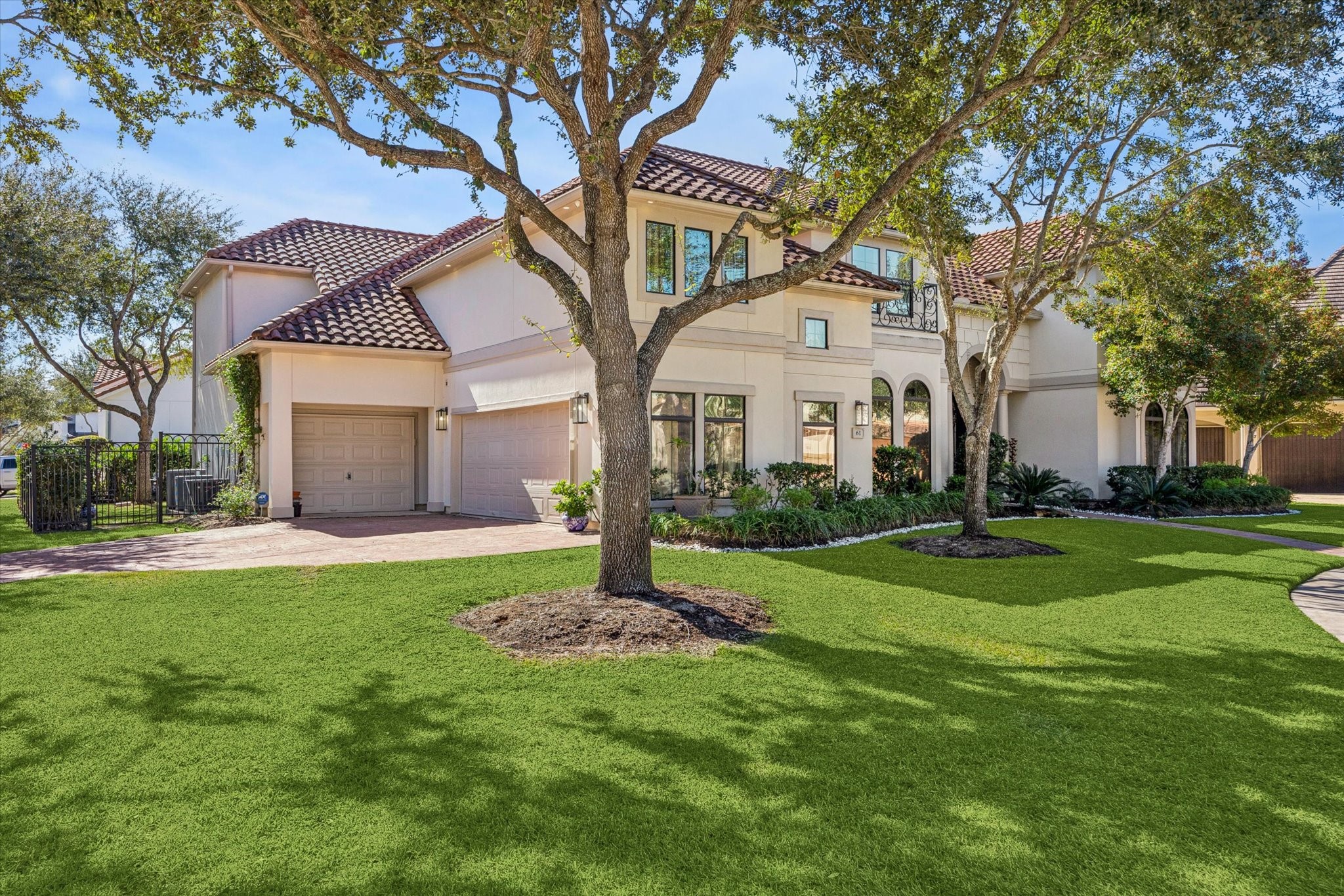 This photo shows a spacious two-story home with a tile roof, large windows, and a well-maintained front yard with mature trees. The driveway leads to a three-car garage Home located on a corner of a cup-de-sac street.