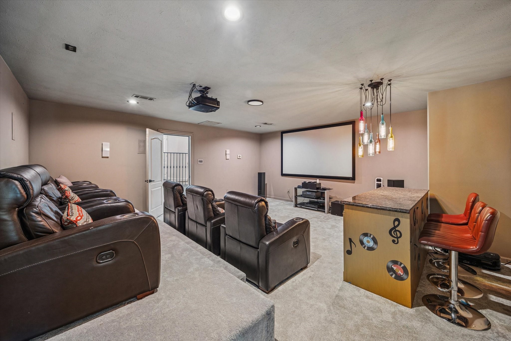 This photo showcases a home theater room with tiered leather recliners, a large projection screen, and a cozy bar area with modern lighting and seating. Perfect for entertaining and movie nights.