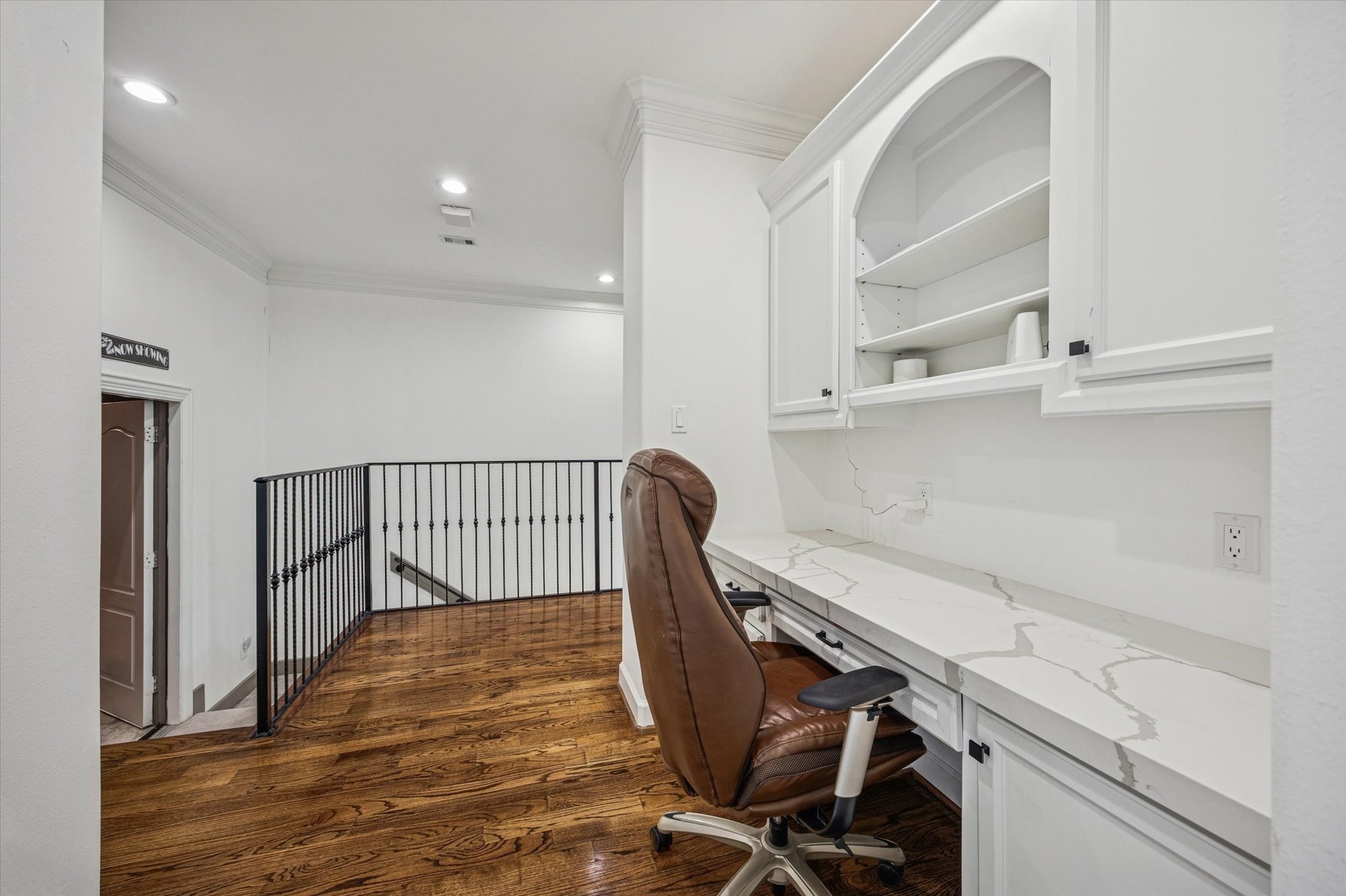 This photo shows a cozy home office nook with built-in white cabinetry and a quartz countertop. The space is well-lit with recessed lighting and has warm wooden flooring.