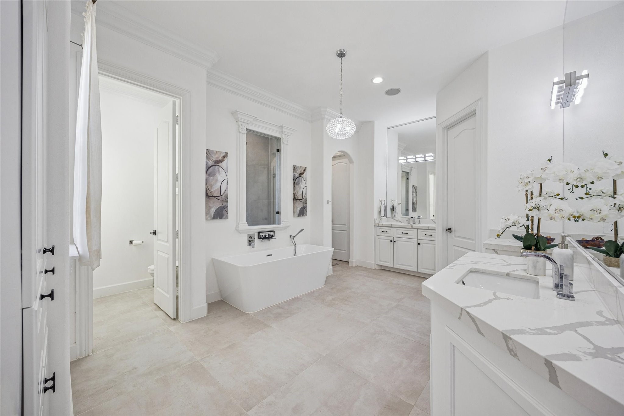 This spacious bathroom features a modern freestanding tub, stylish dual vanities with marble countertops, and elegant lighting. The neutral tones and ample natural light create a relaxing, spa-like atmosphere.