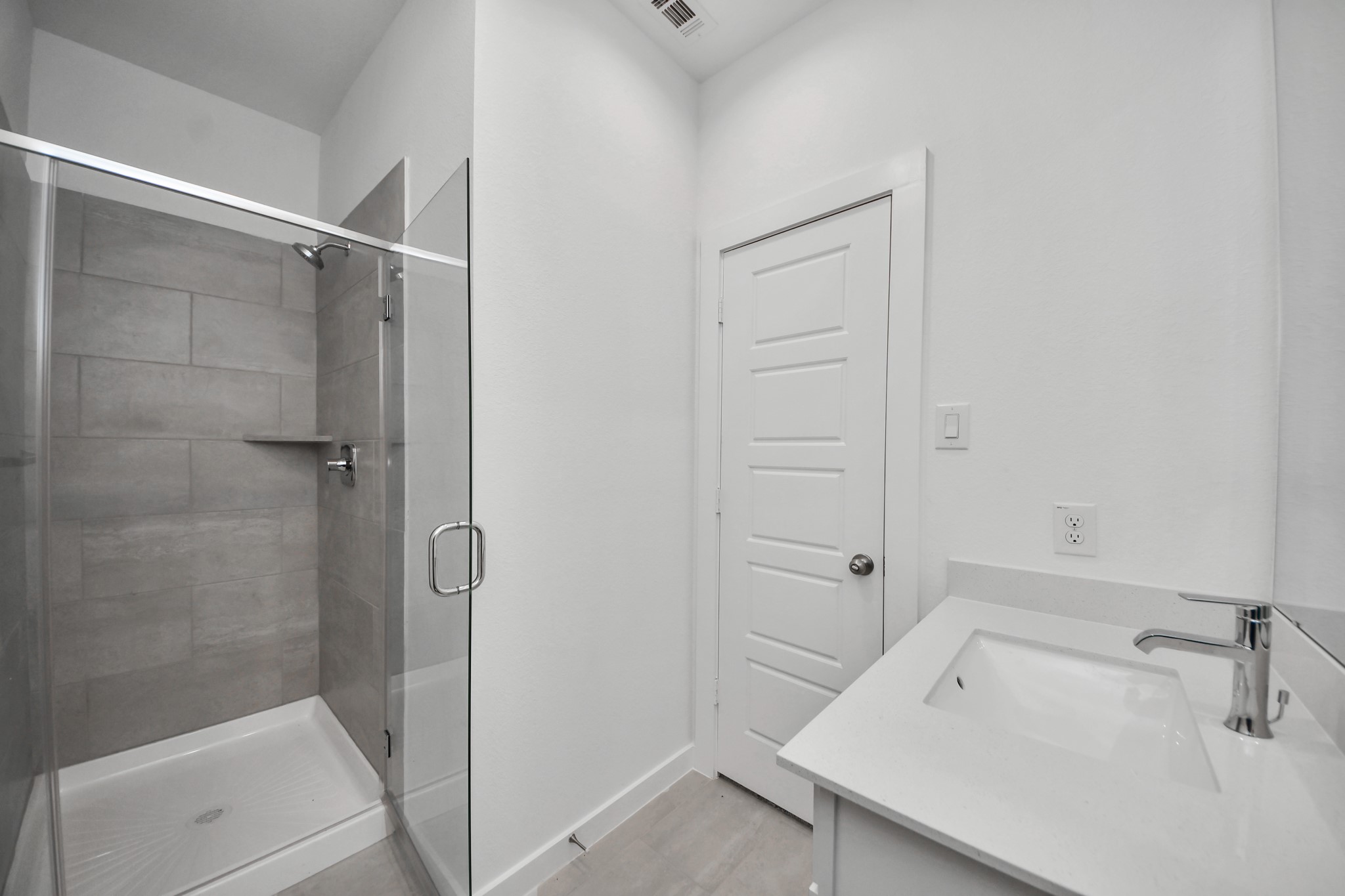 Secondary bath features tile flooring, walk-in shower with tile surround, light stained wood cabinets, beautiful light countertop.