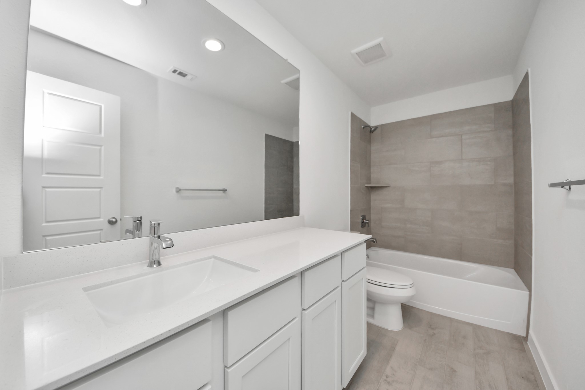 Secondary bath features tile flooring, bath/shower combo with tile surround, light stained wood cabinets, beautiful light countertop.