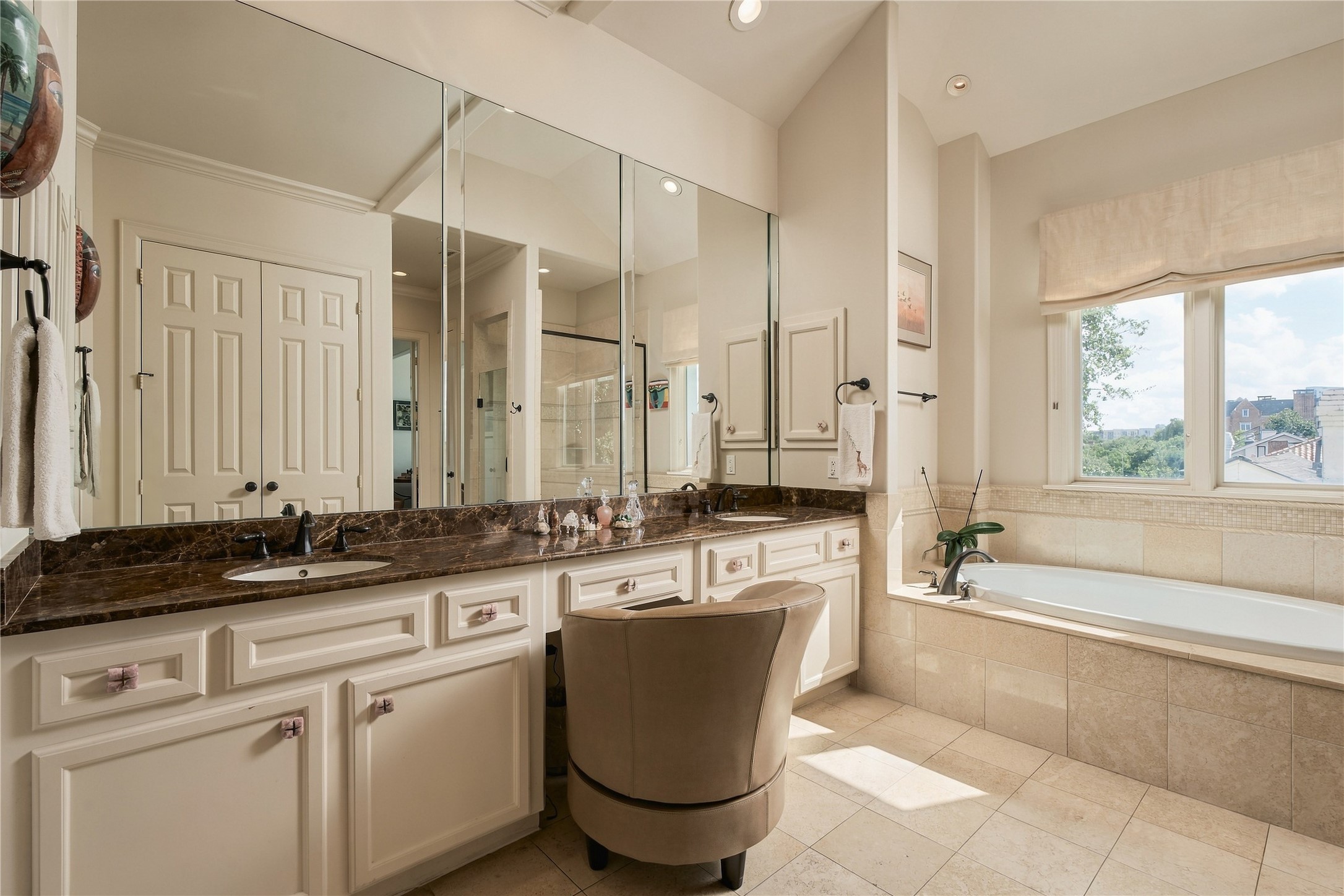 Natural light fills the primary bath, highlighting the expansive vanity, warm stone finishes and generous storage.