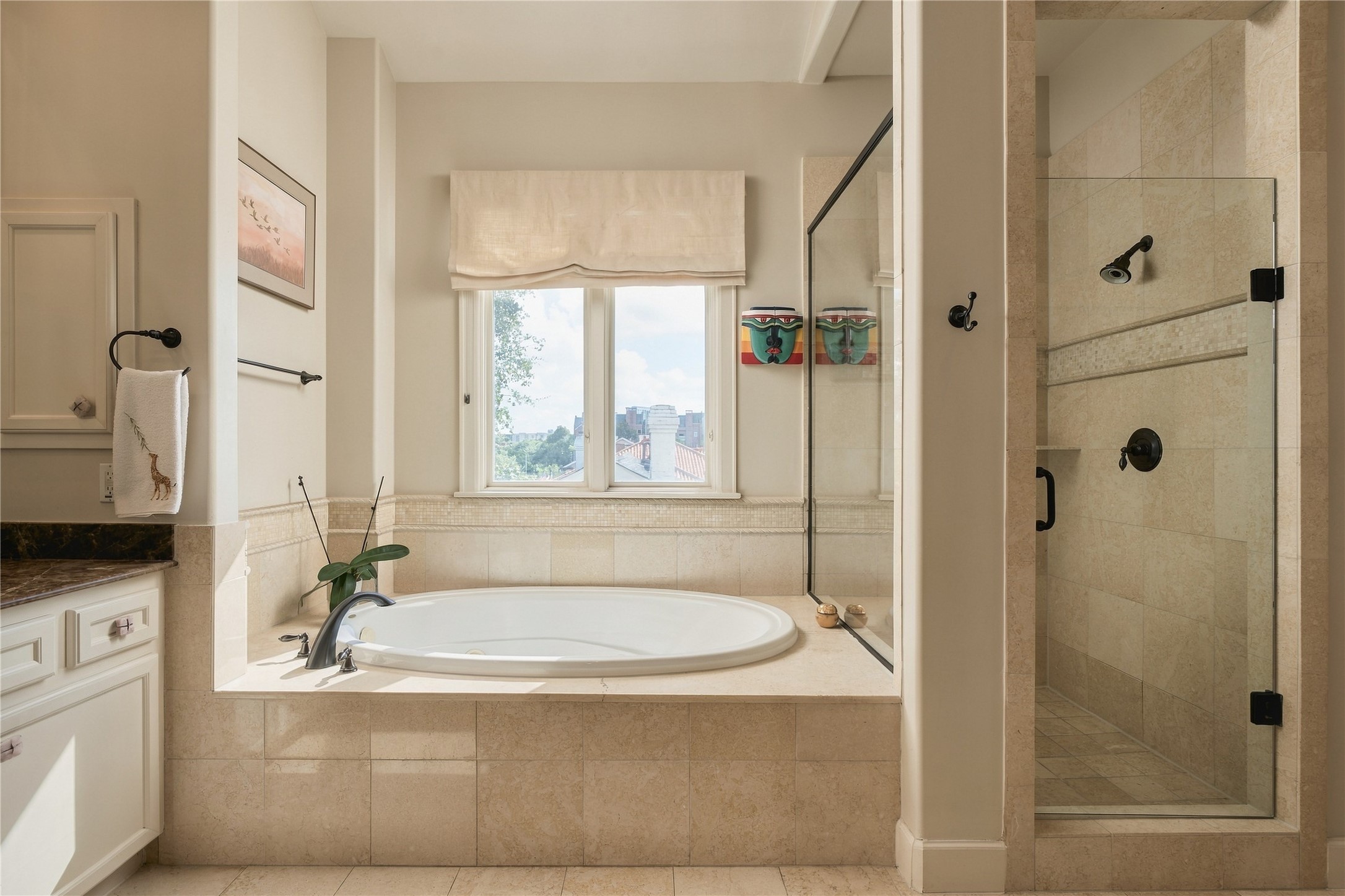 A jetted soaking tub and separate glass-enclosed shower create distinct spaces to slow down or get ready for the day, with natural light bringing warmth into the stone-finished bath.