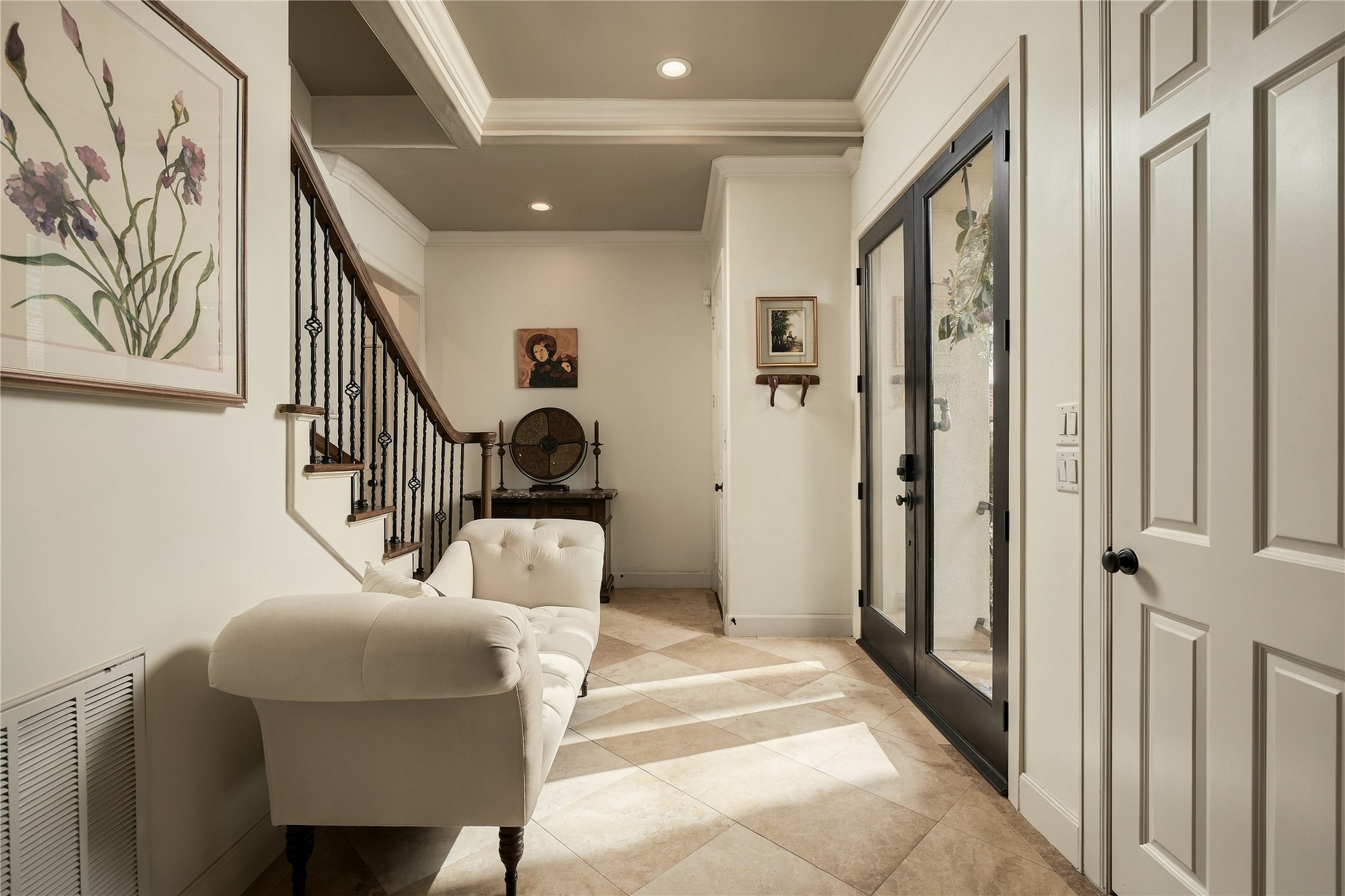 Step inside and the pace immediately changes. The entry feels warm and collected, with natural light coming through the glass doors and the staircase beginning the journey upward.