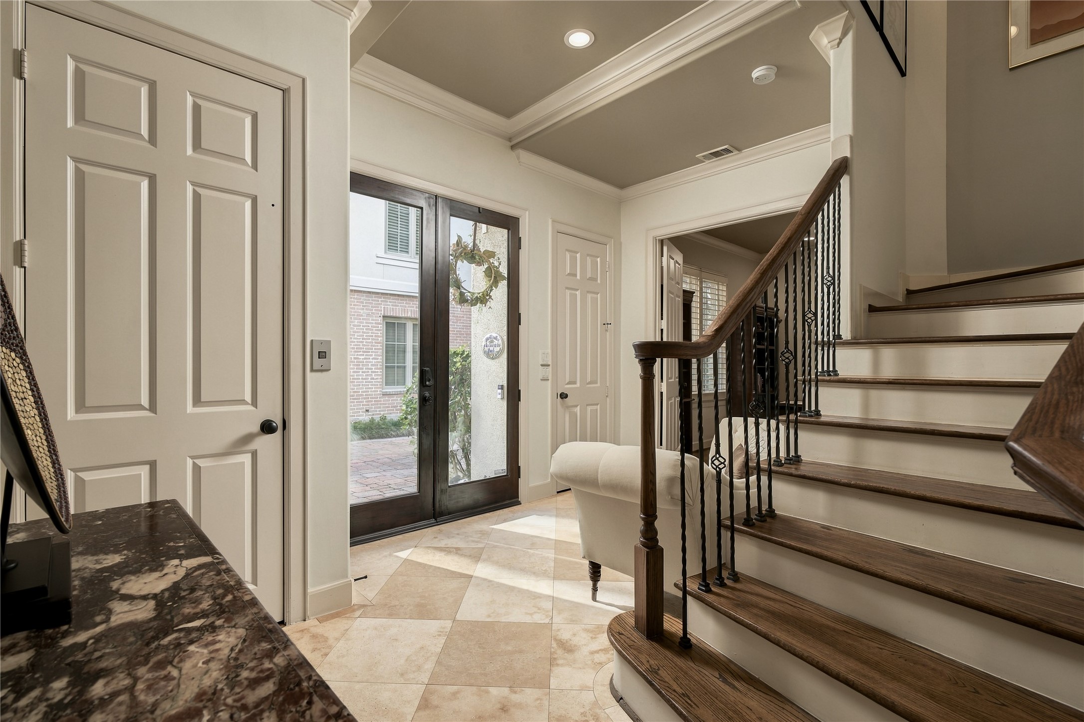 Back in the entry, the staircase becomes part of the architecture, pairing warm wood with iron detailing as the home begins to unfold vertically.